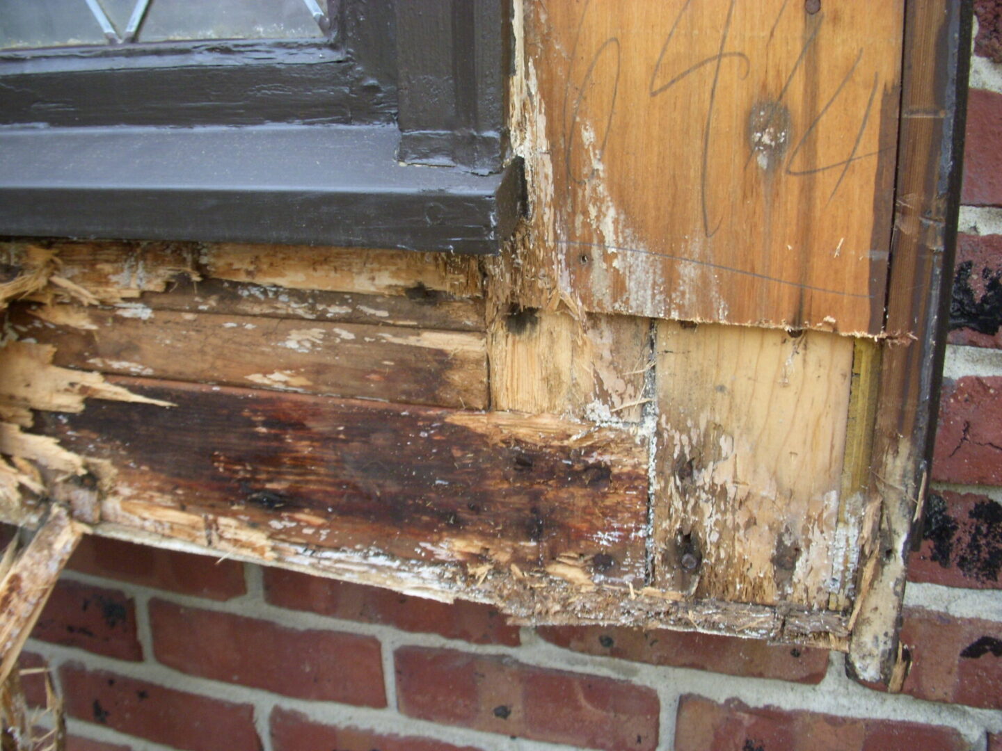 Close-up of rotting wood near a window frame on a brick wall.