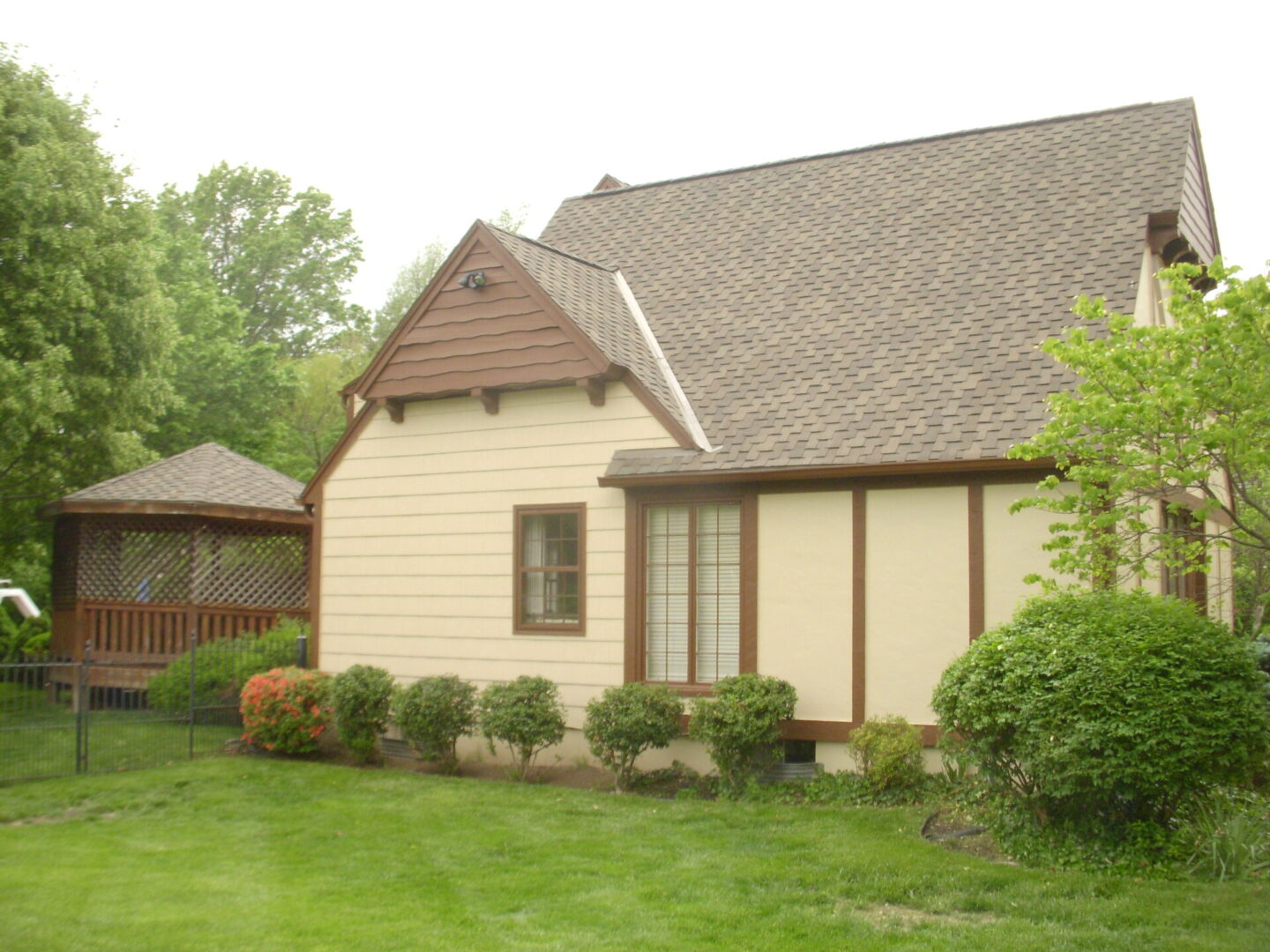 A beige house with a brown roof and neatly trimmed bushes in the front yard.