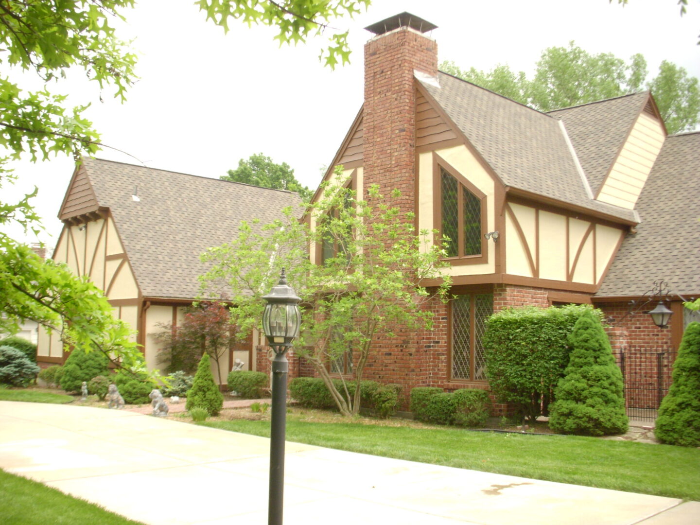 Charming Tudor-style home with a brick chimney and lush greenery.