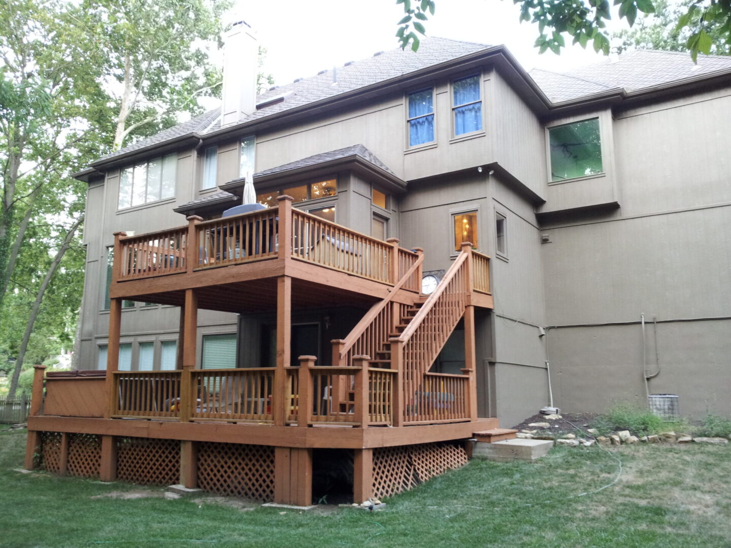 A two-story house with a wooden deck and staircase in the backyard.