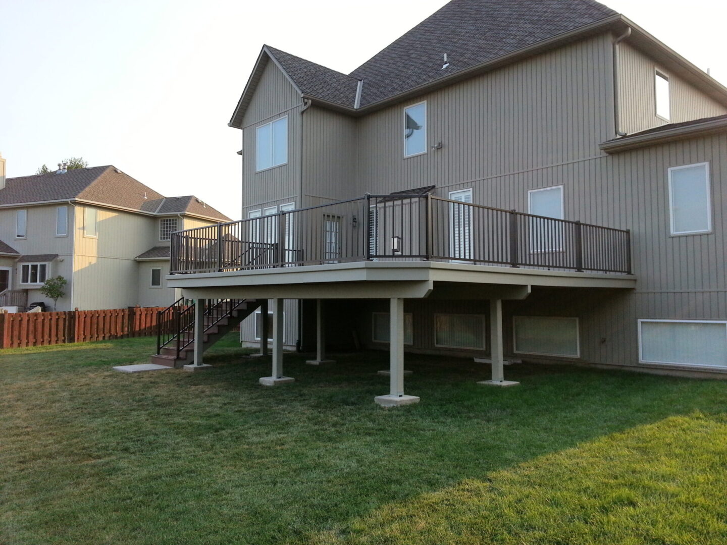 A raised wooden deck attached to a house with a grassy backyard.