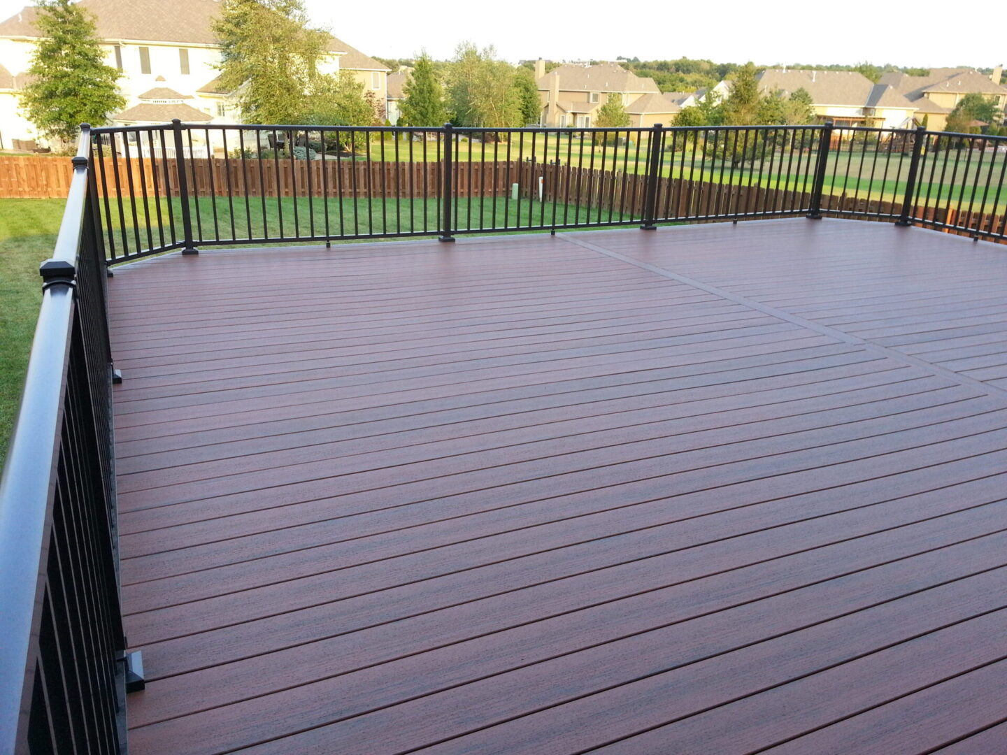 Spacious wooden deck with black metal railing overlooking a green lawn.