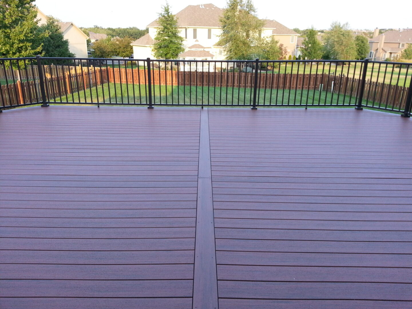 Spacious wooden deck with black metal railing overlooking a green backyard.
