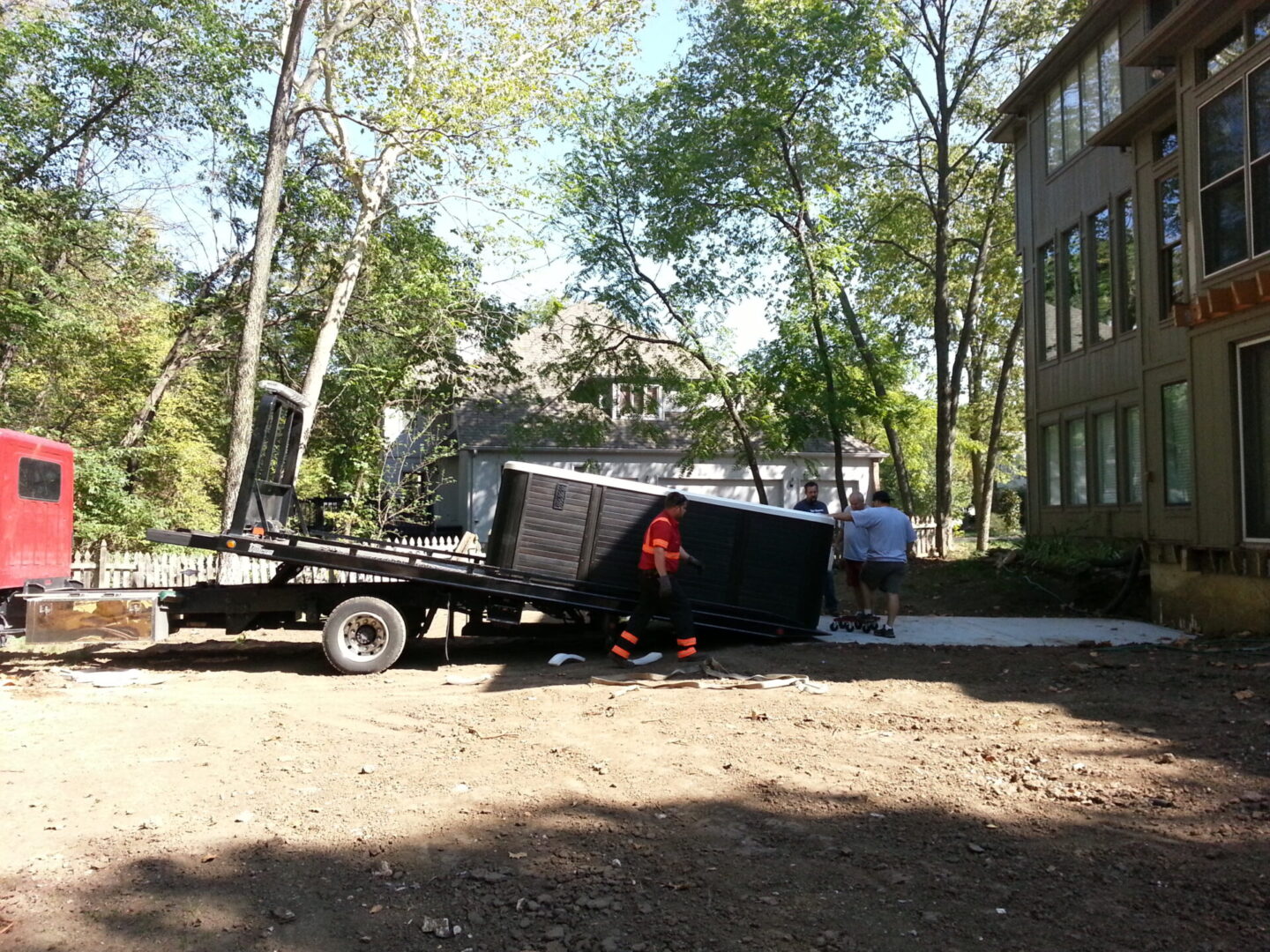 Workers unloading a large black container from a truck in a wooded area.
