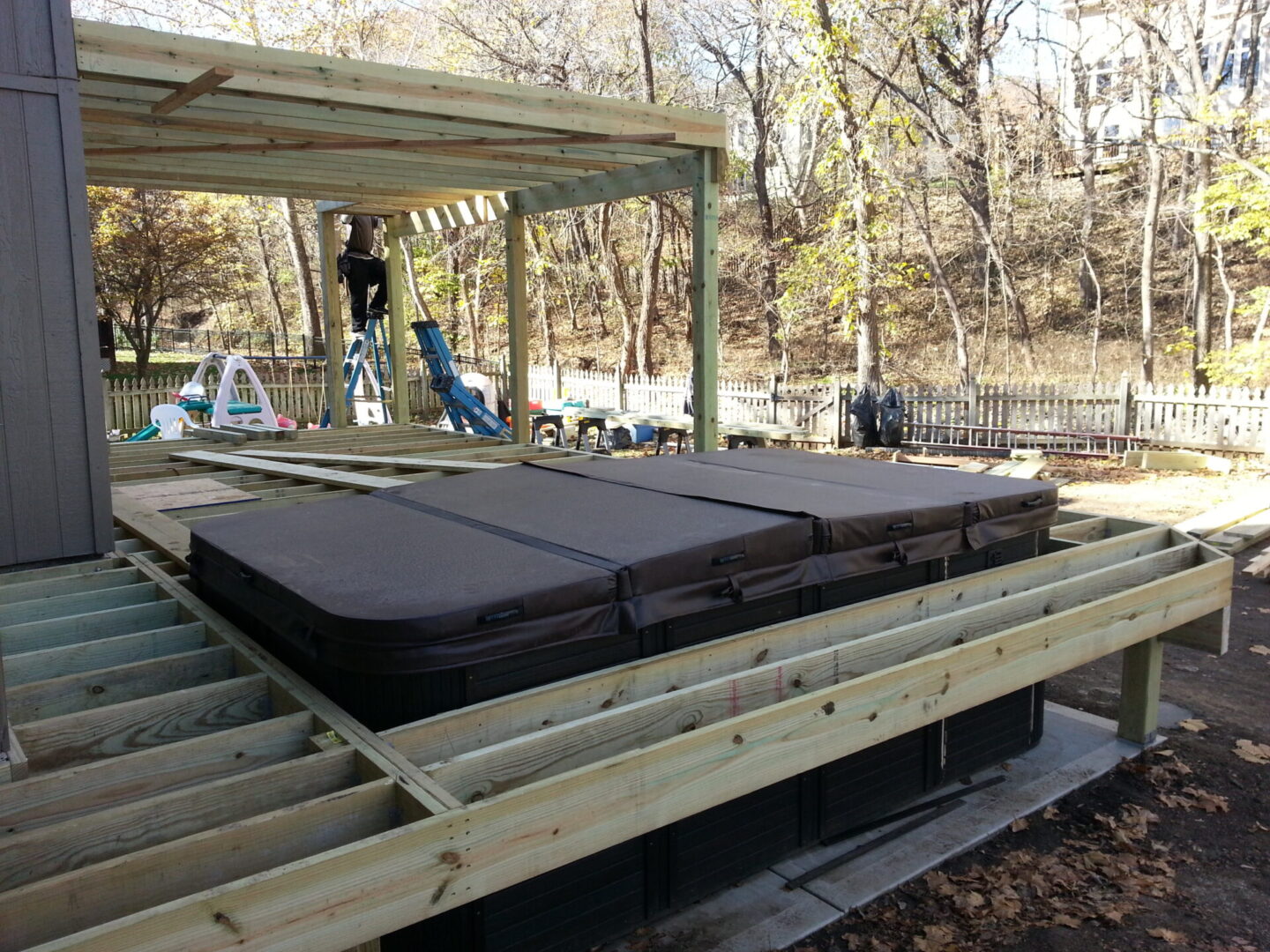A large black hot tub installed on a wooden deck in a wooded area.