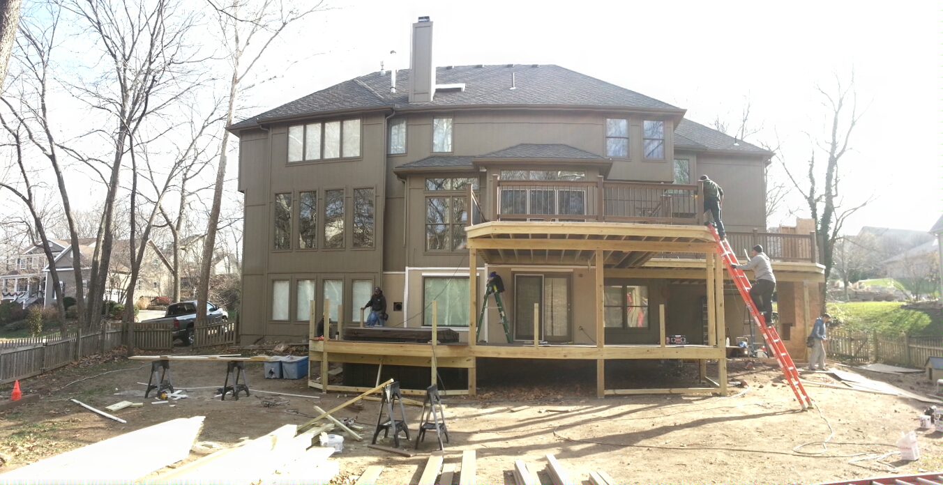 Large multi-story house with a wooden deck under construction in the backyard.