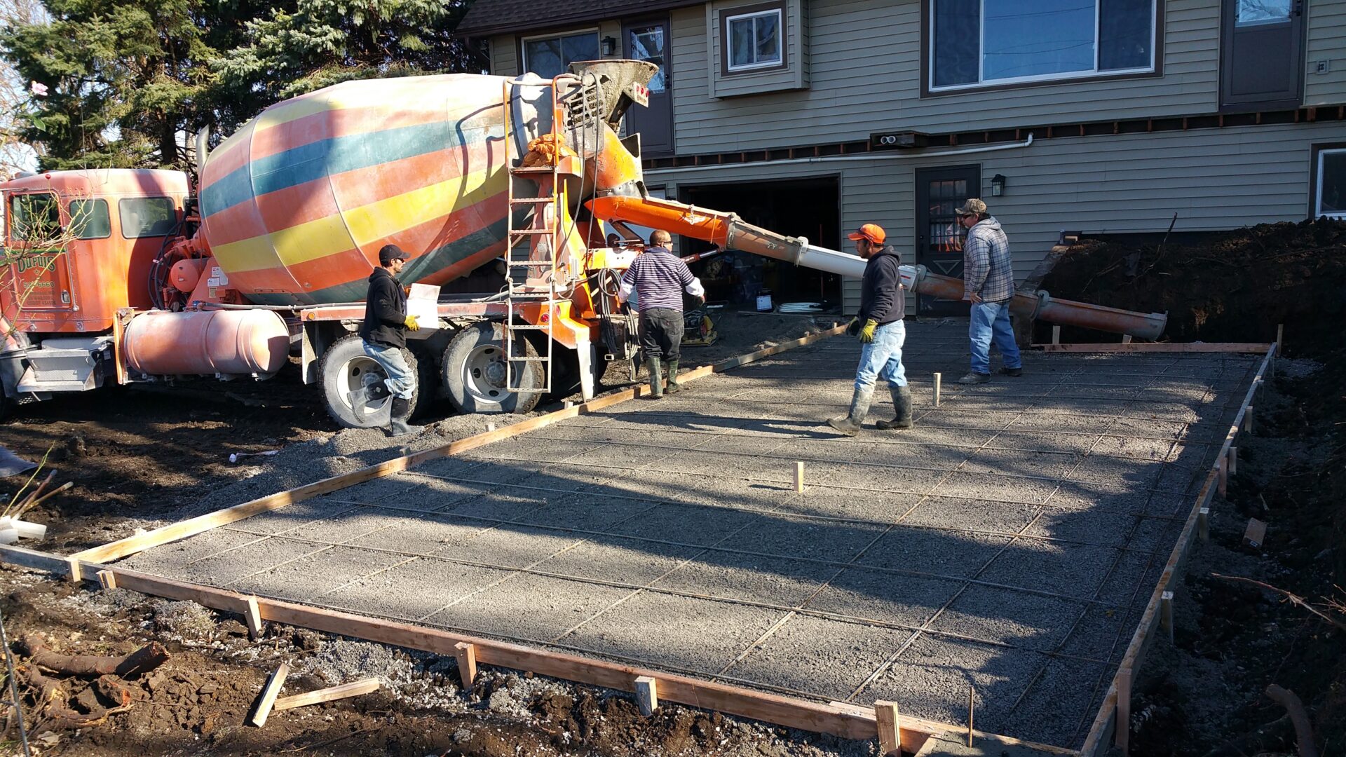 Workers pouring concrete from a mixer truck to form a slab.