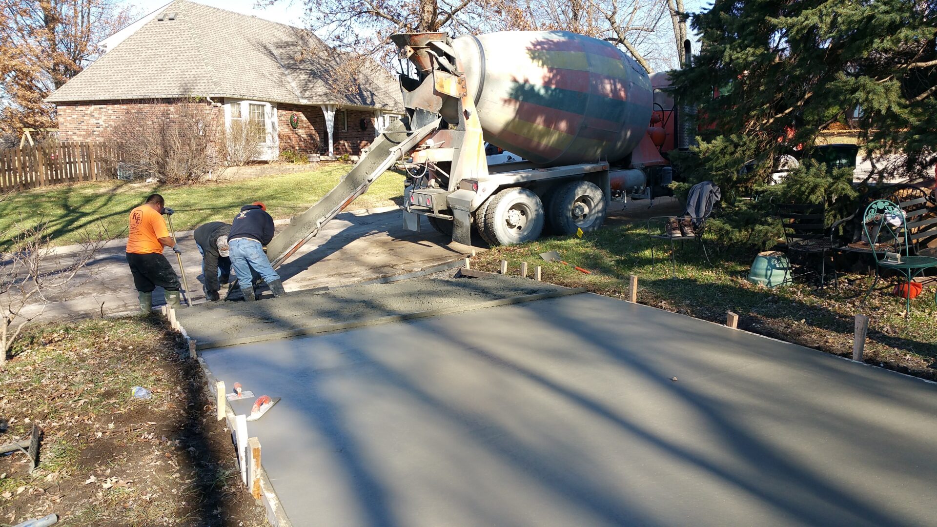 Workers pouring concrete from a mixer truck on a sunny day.