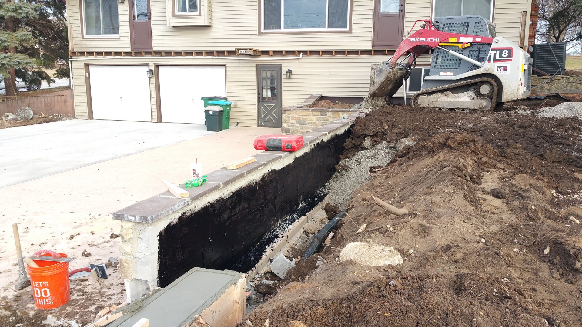 A house foundation is being waterproofed with black coating.