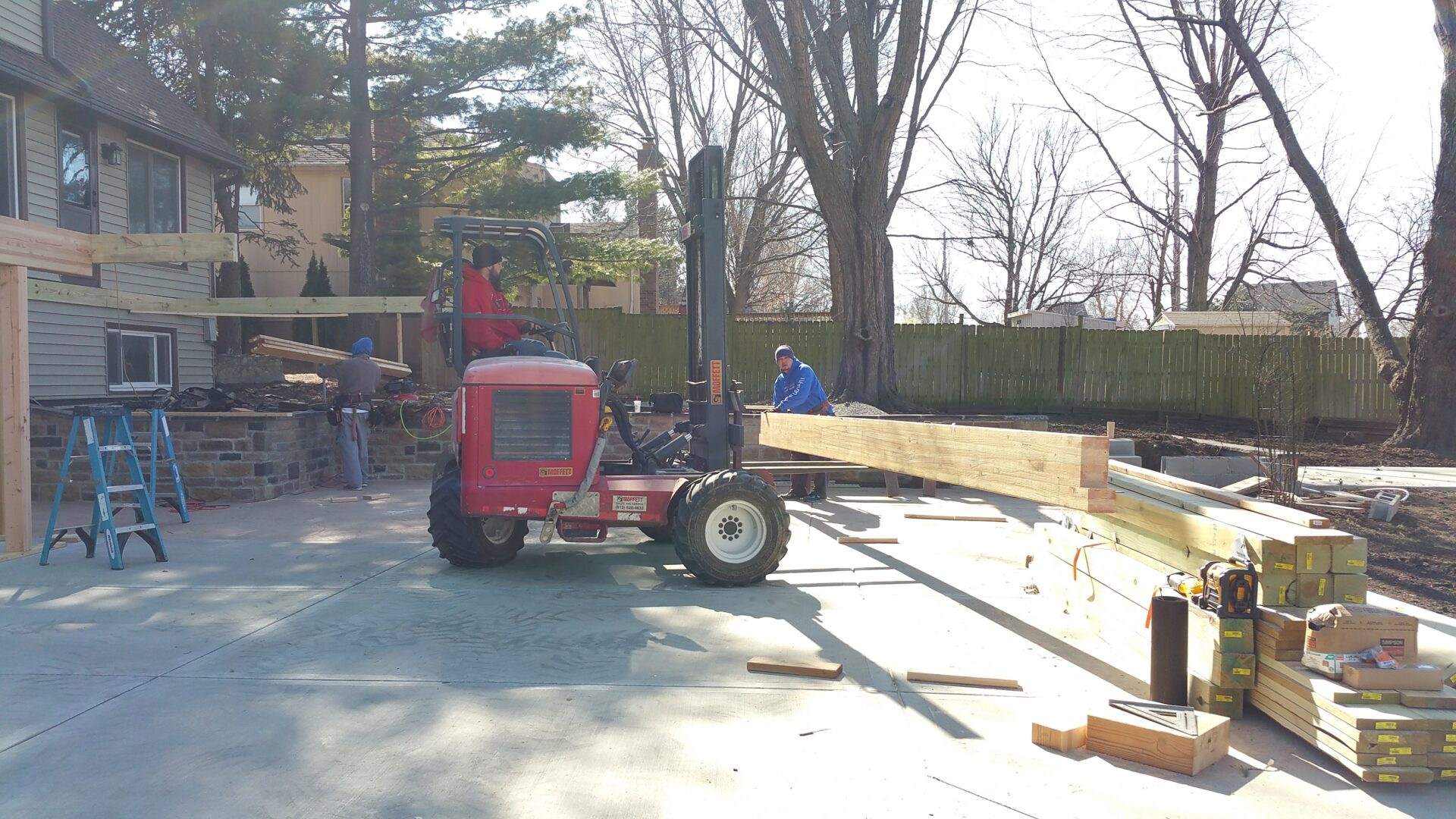 Workers using a small forklift to lift lumber at a construction site.