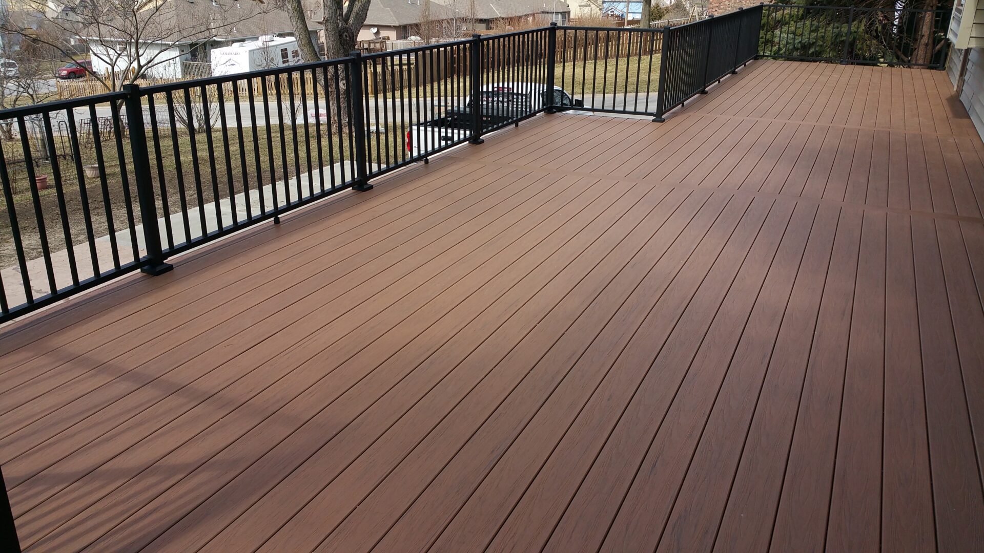 A spacious brown wooden deck with black metal railings overlooking a water body.