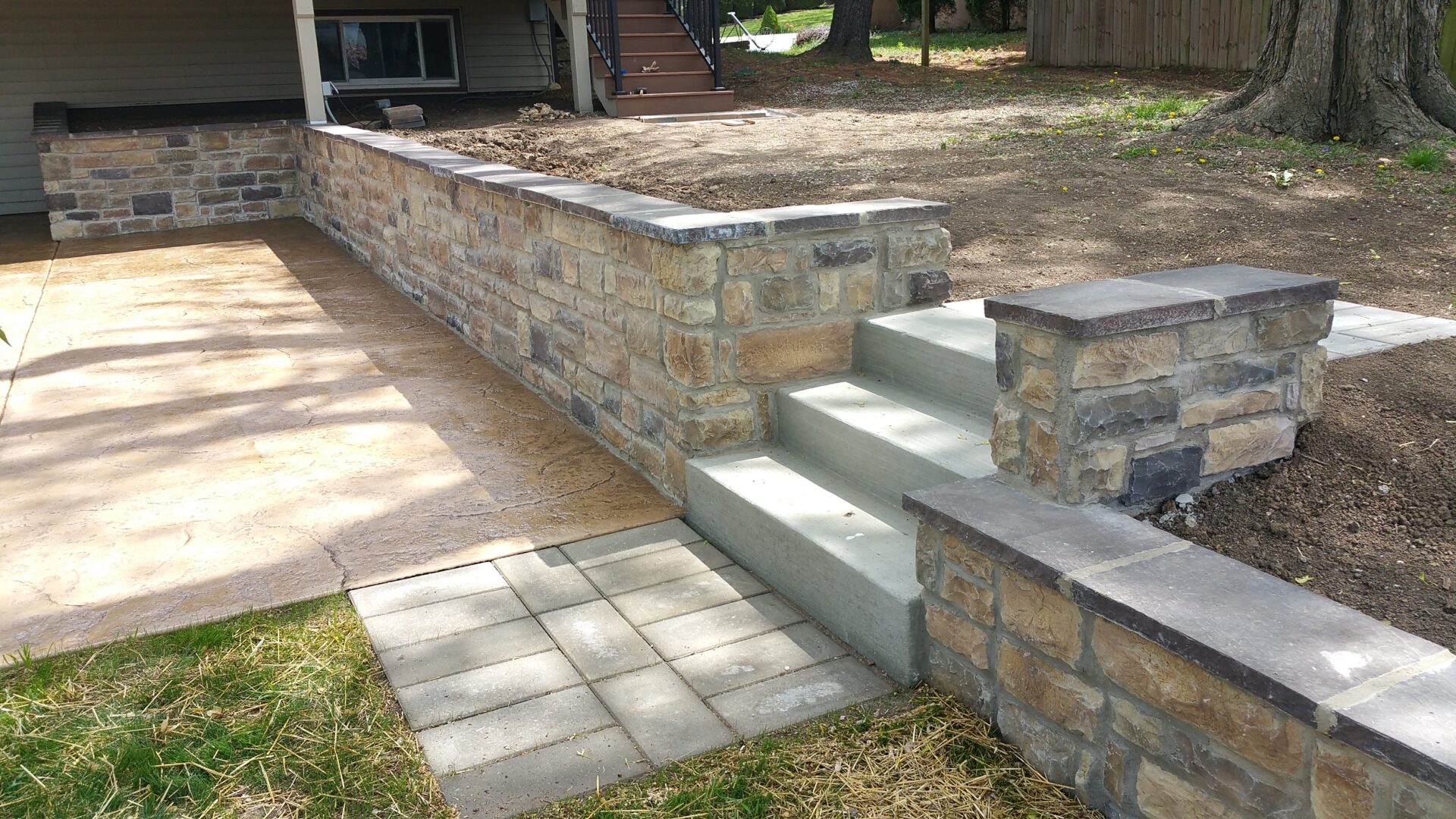 Stone retaining wall with concrete steps and a paved walkway.