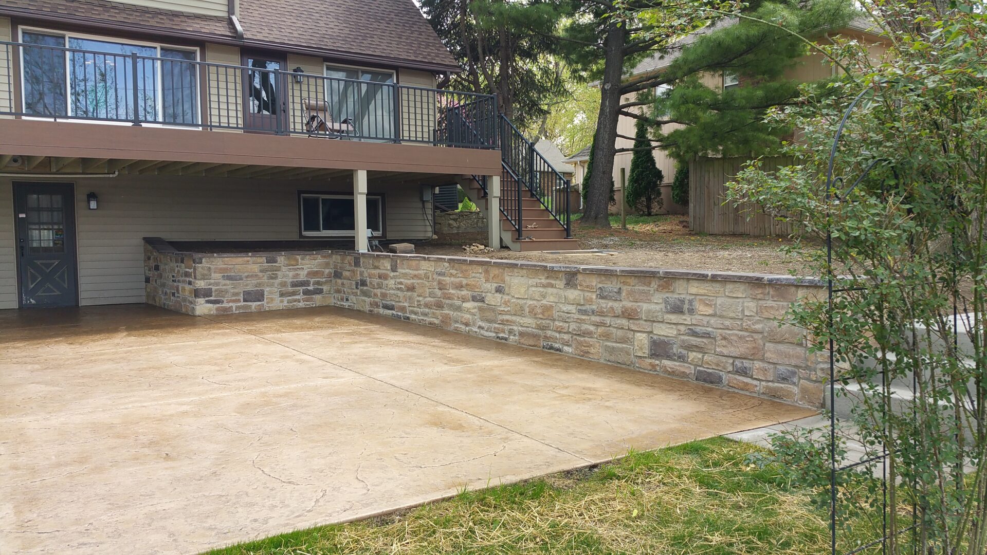 A backyard with a concrete patio and a stone retaining wall.