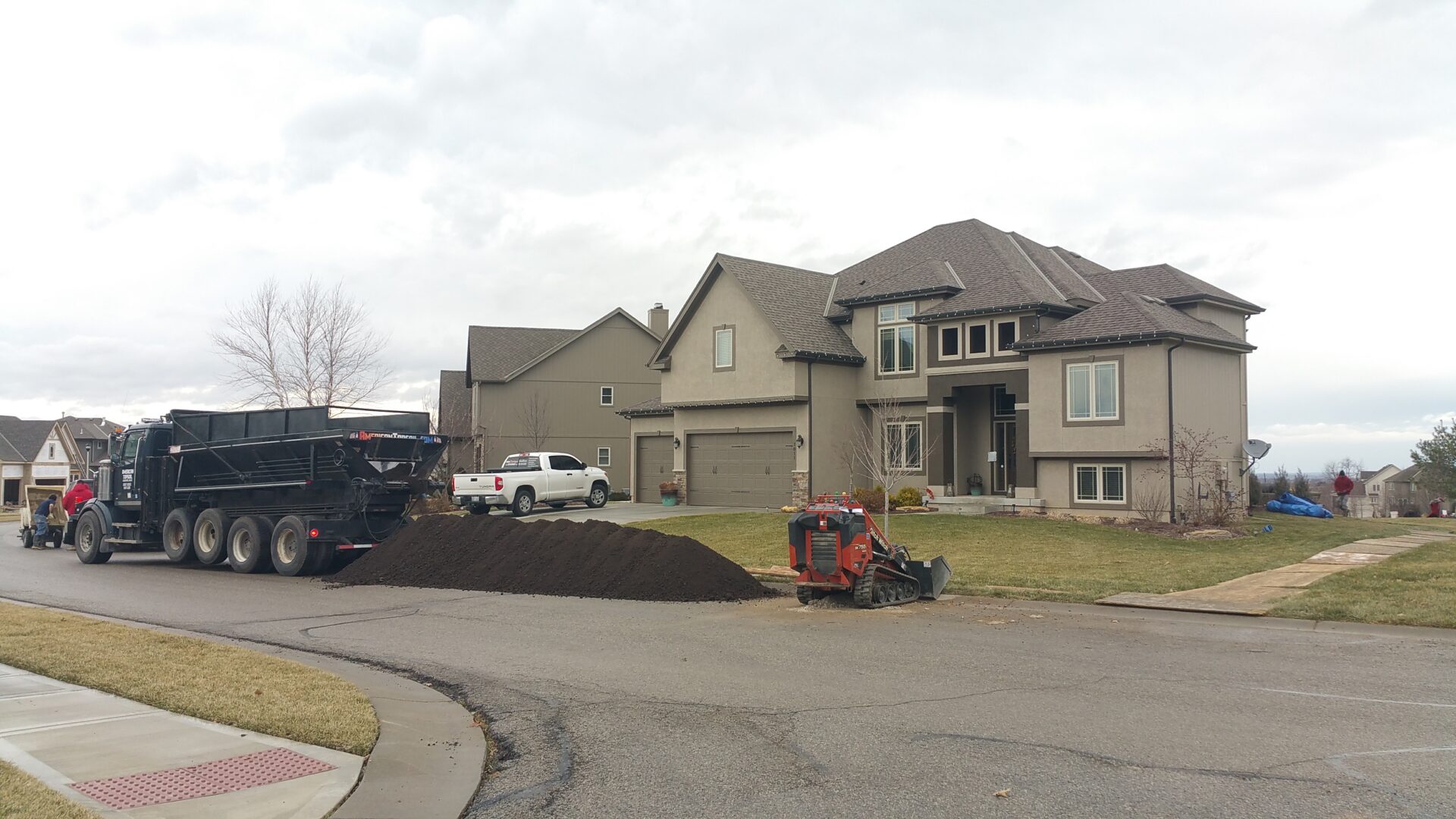 Residential street with a large pile of soil and construction vehicles.
