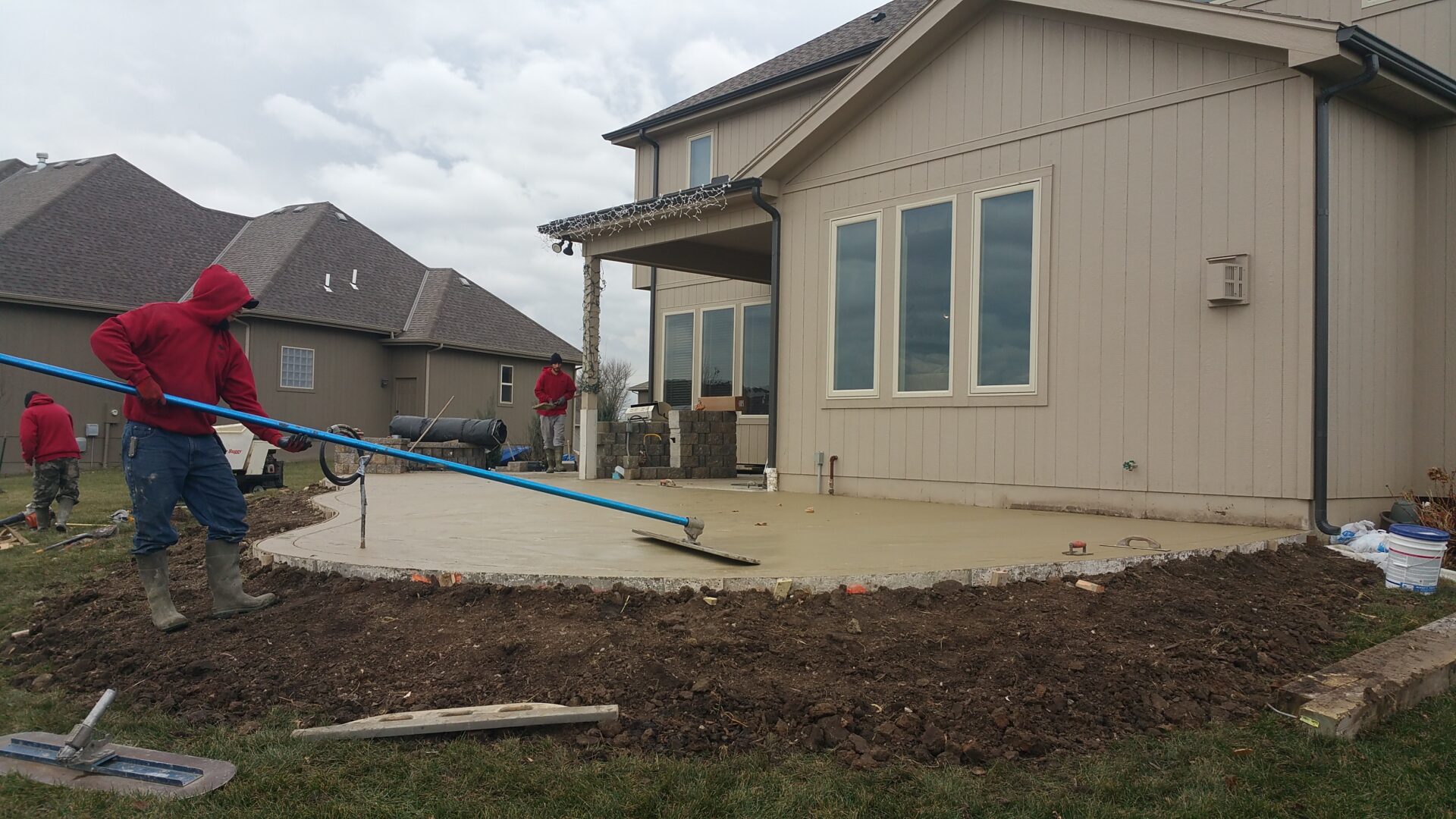 Newly poured concrete patio beside a beige house under a cloudy sky.