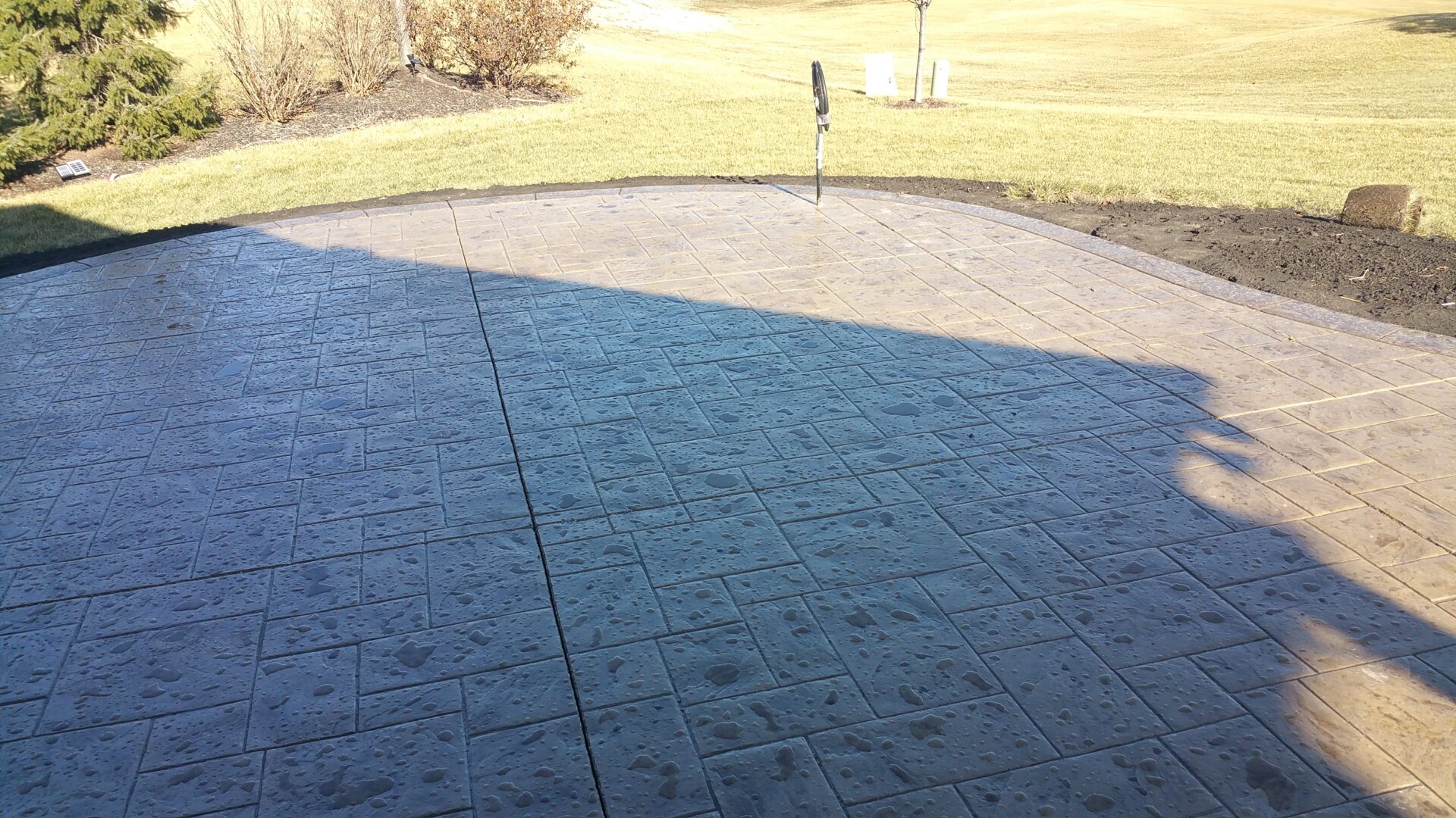 Sunlit patio with shadow dividing grassy area and stamped concrete.