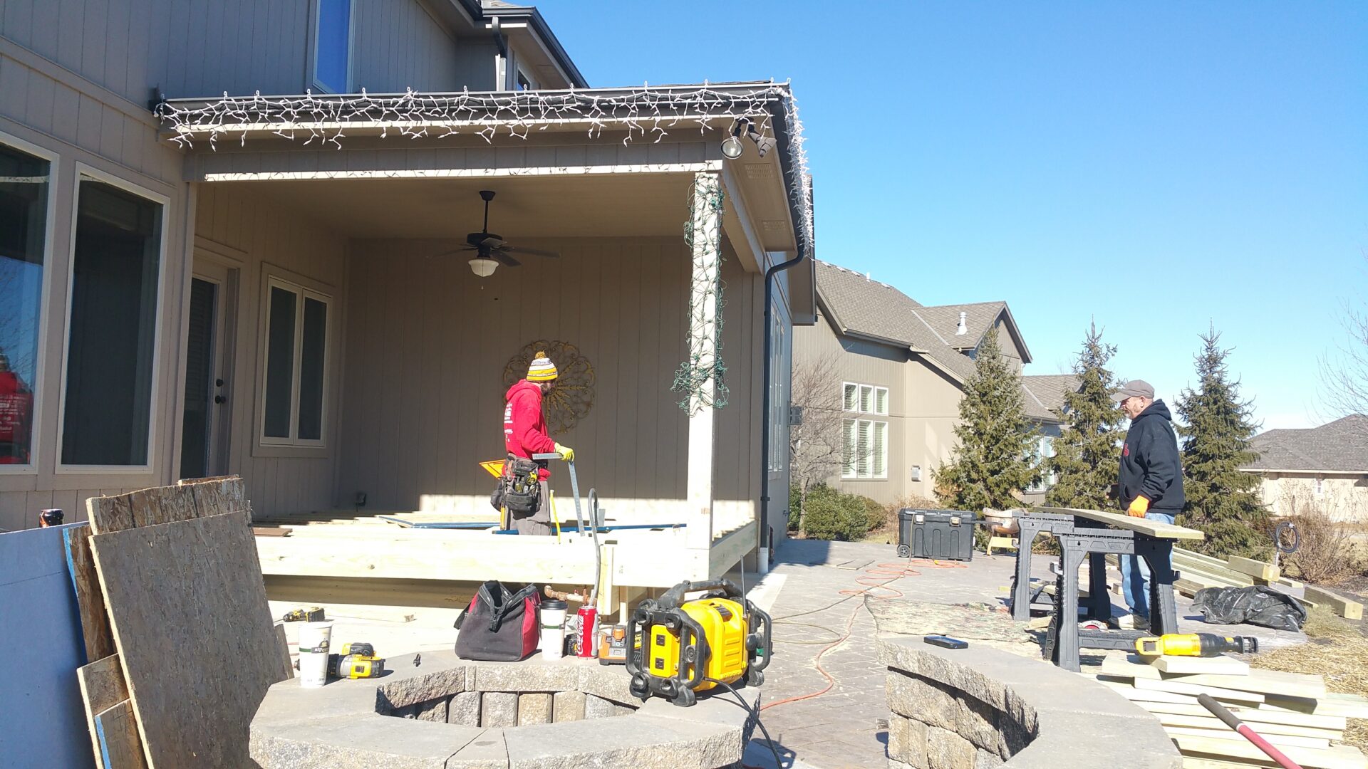 Construction worker working on a residential porch under a clear blue sky.