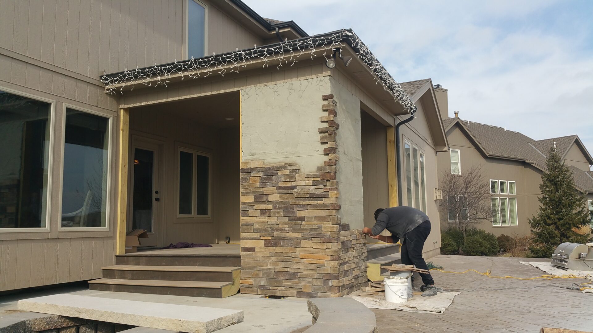 Worker applying stone veneer on house exterior corner.
