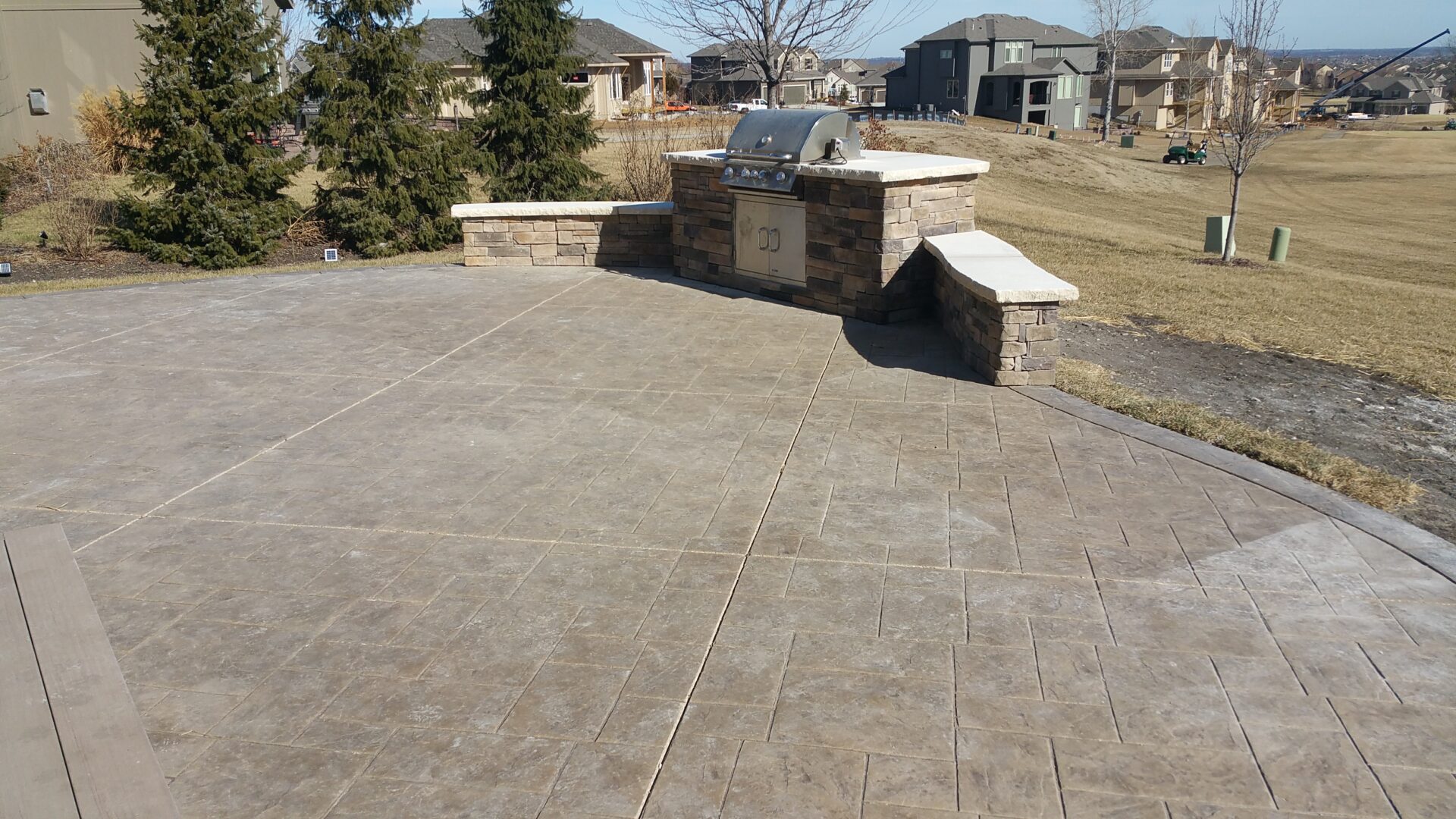 Stone bench and mailbox on a paved patio in a suburban neighborhood.