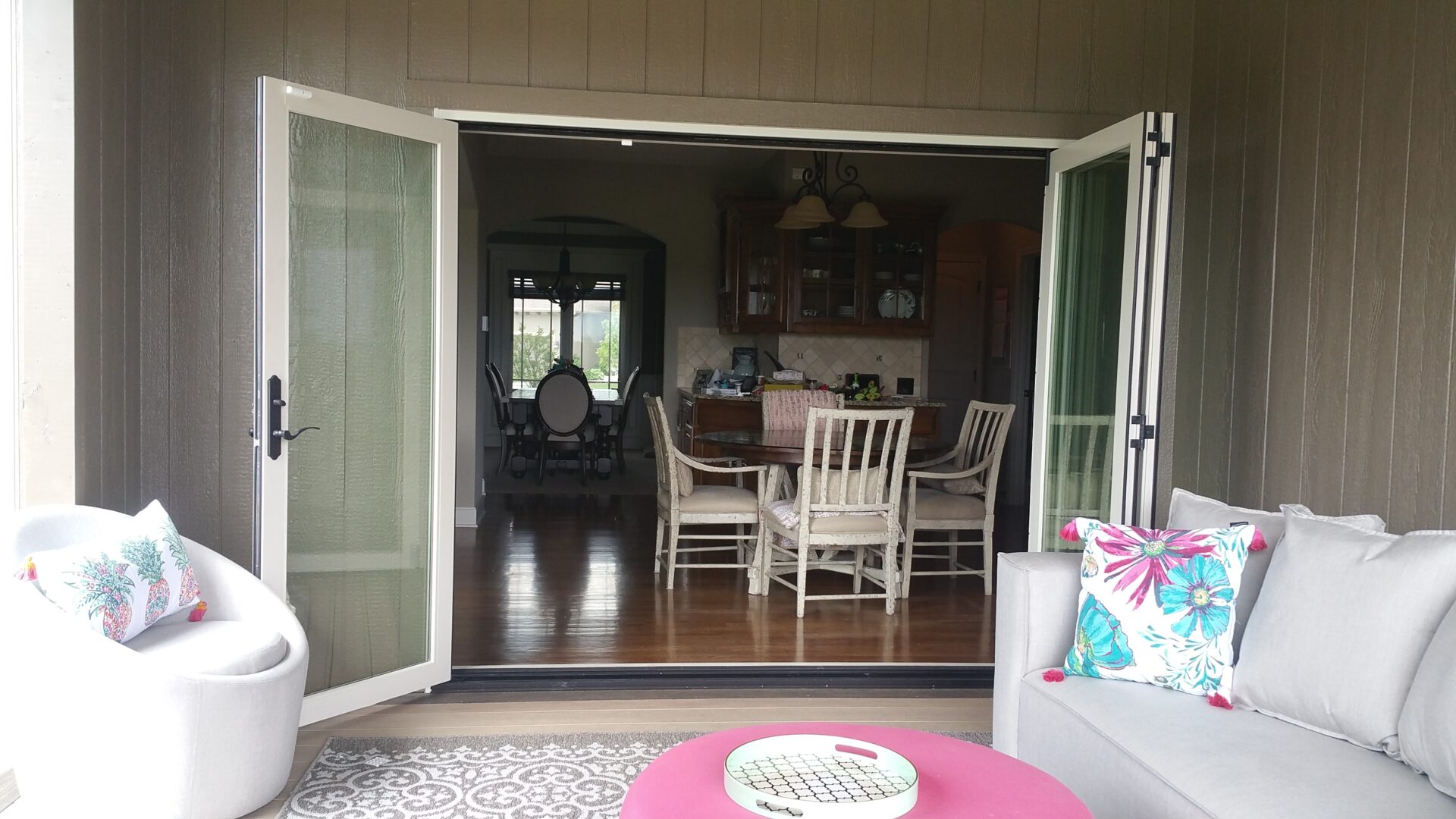 Open dining area with white chairs and wooden table seen from a porch.