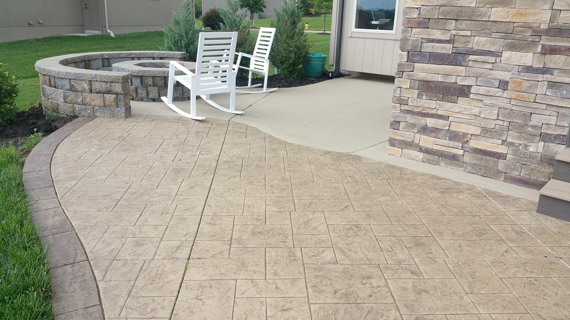 Outdoor patio area with stamped concrete and white chairs.