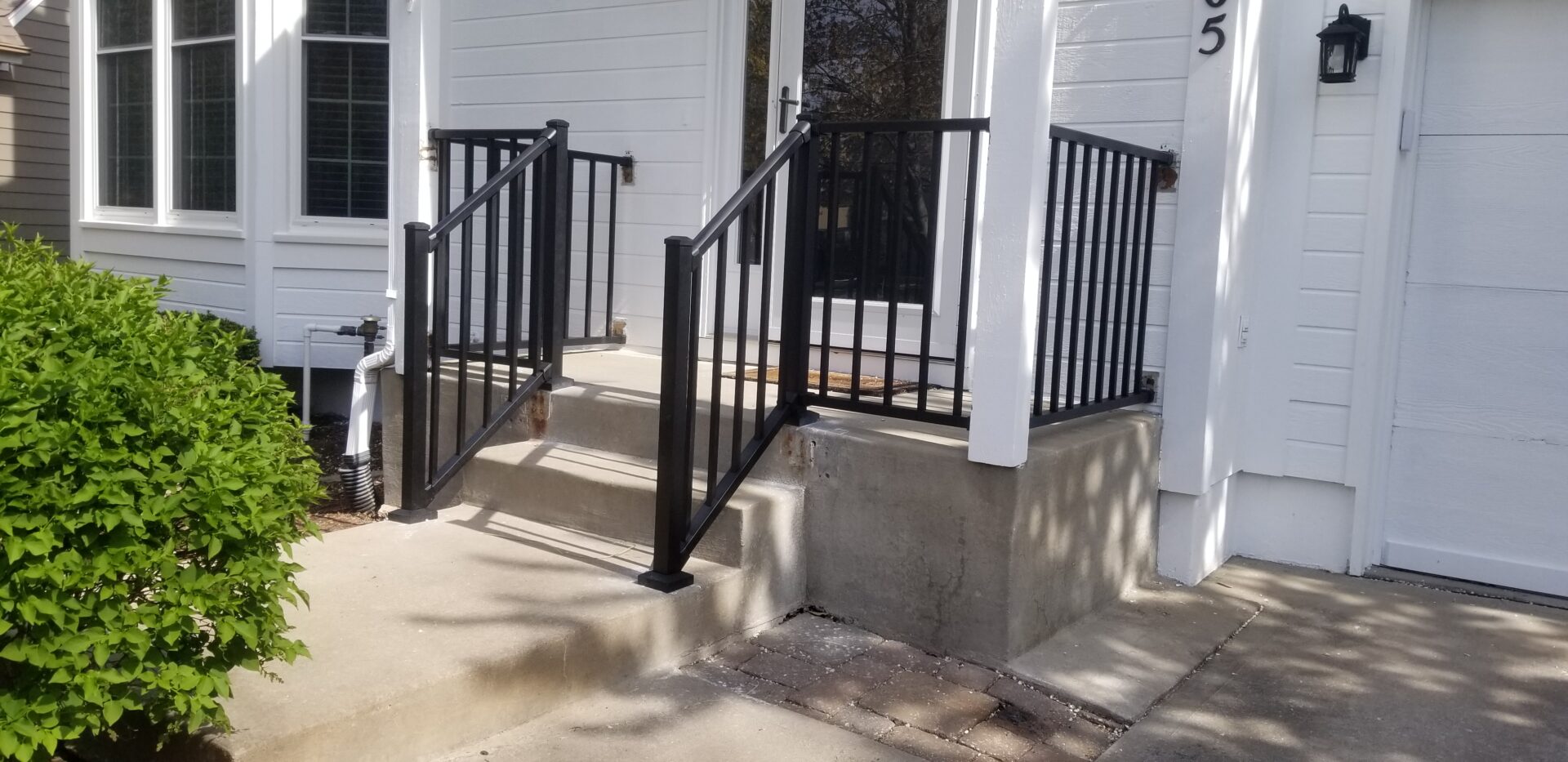 Sturdy black metal handrails installed on concrete steps leading to a white building entrance.