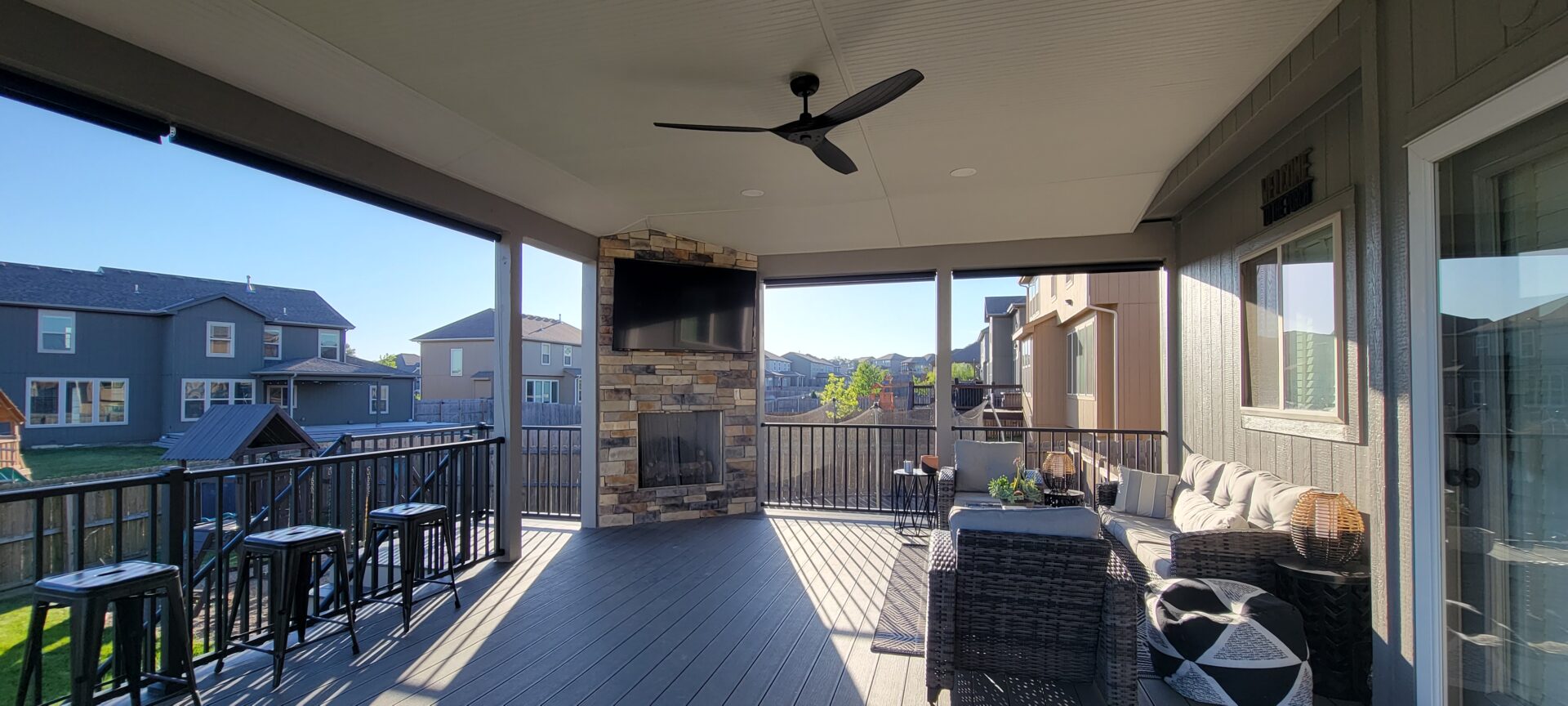 Cozy outdoor patio with ceiling fan and TV overlooking neighboring houses.