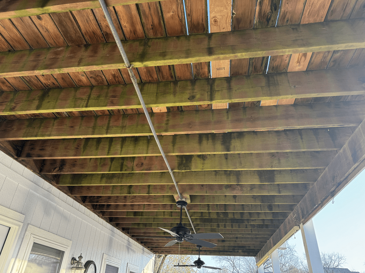 Wooden ceiling with beams and ceiling fans under a porch.