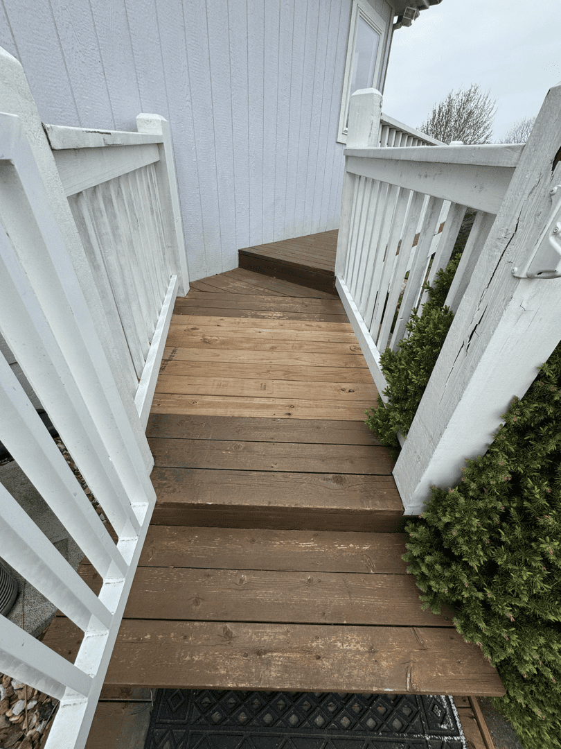 Wooden stairs with white railings and greenery on the side.