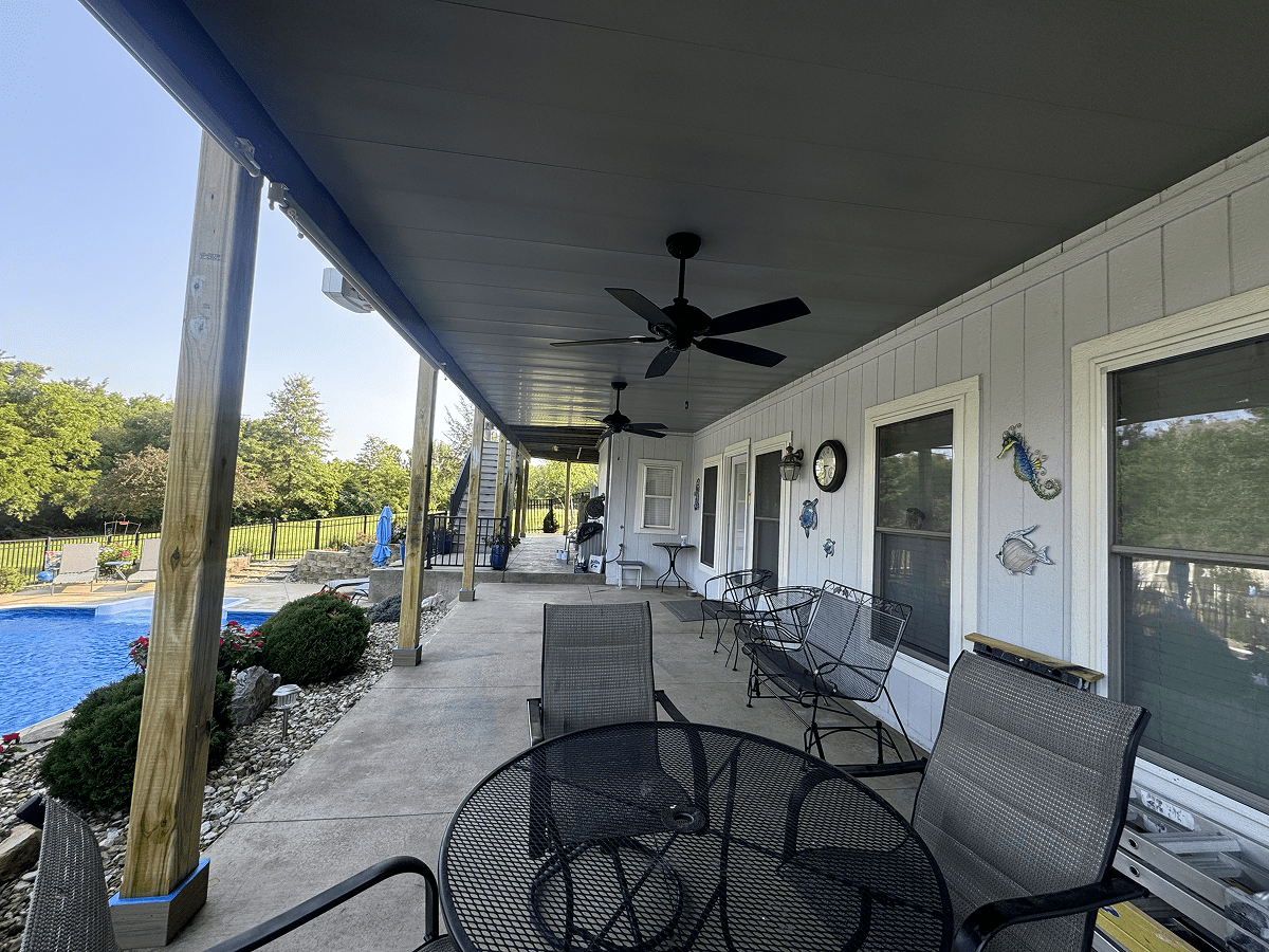 Spacious outdoor patio with seating and ceiling fans overlooking a garden.