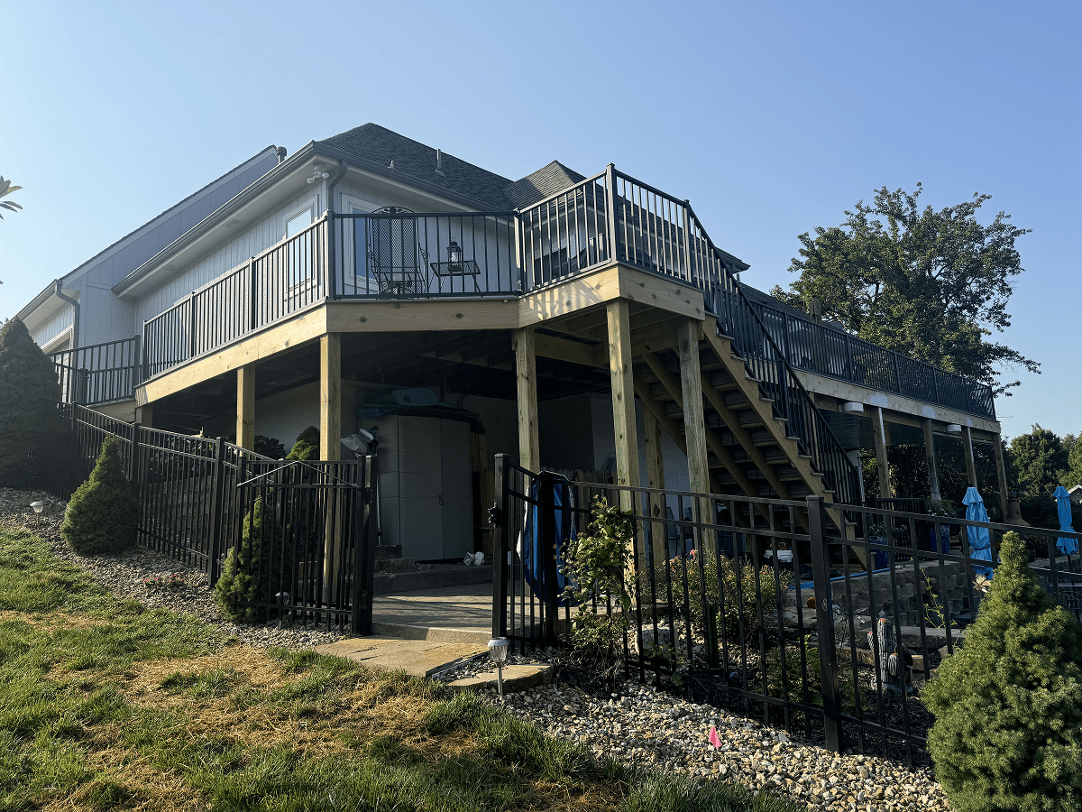 A two-story house on stilts with an outdoor staircase and fenced yard.