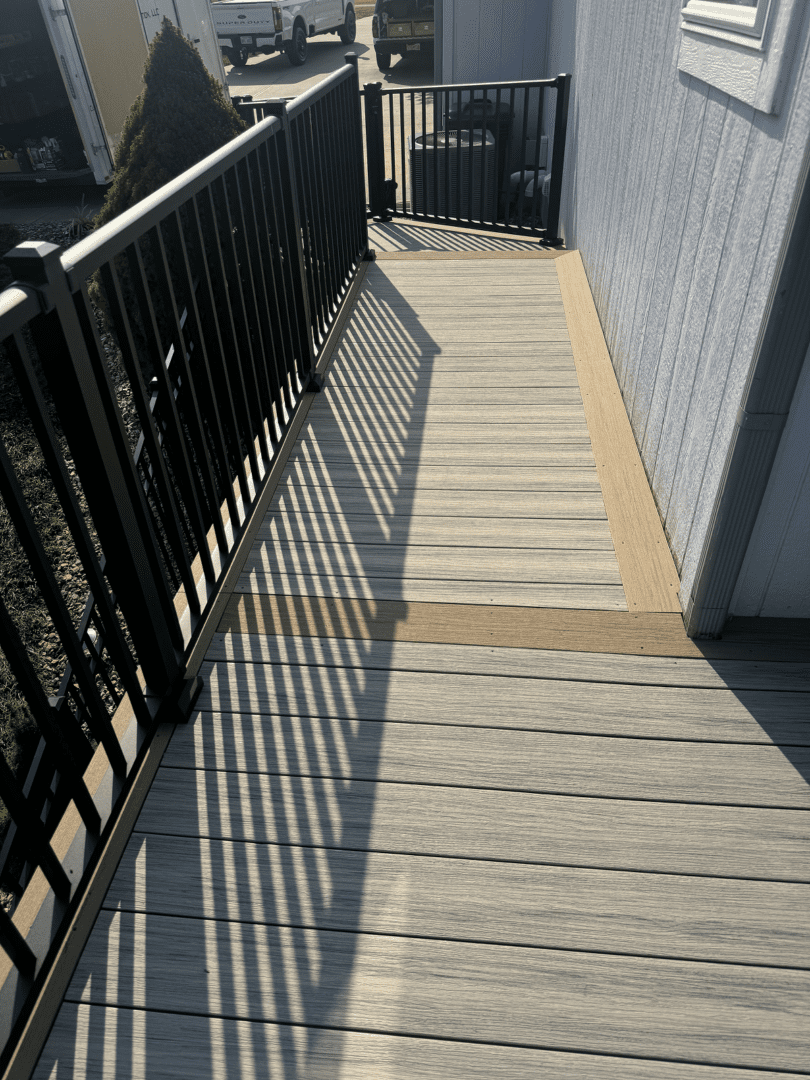 Sunlight casts shadows of railings on a textured concrete walkway beside a building.