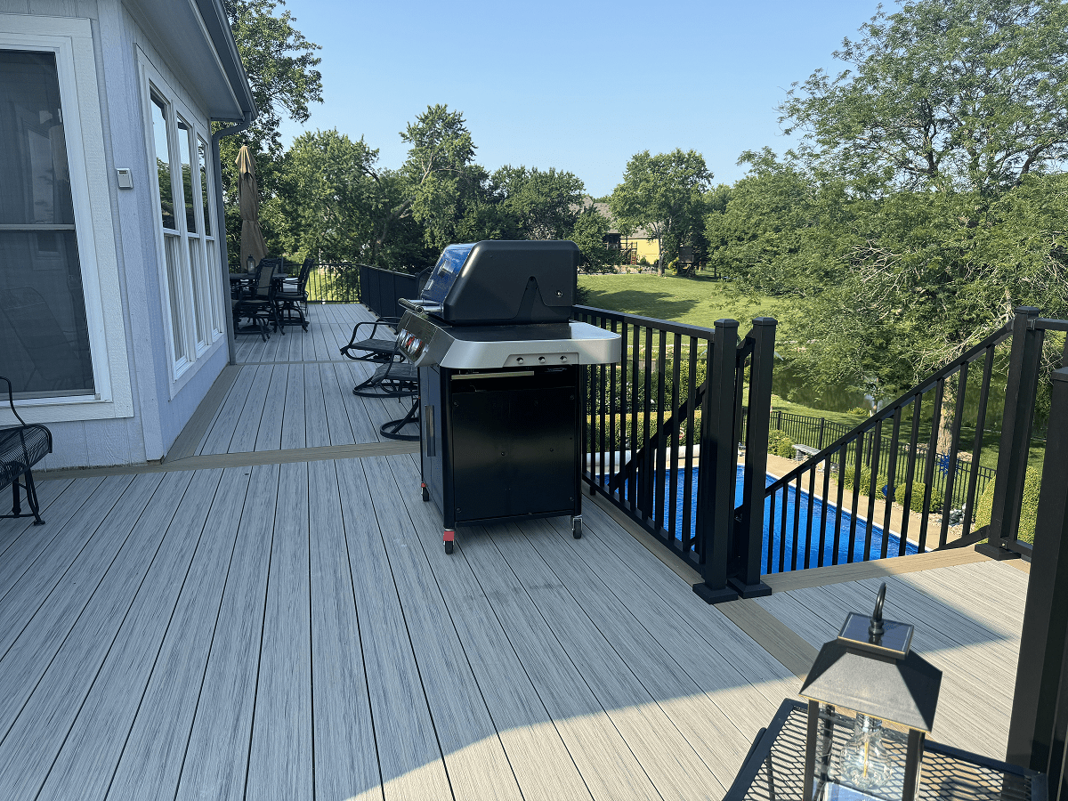Backyard deck with a grill, chairs, and a view of a green yard.