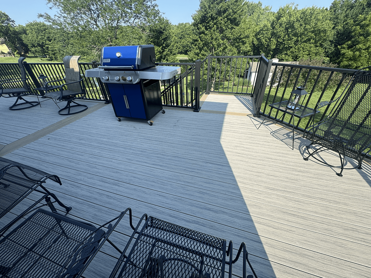 Spacious backyard deck with grill and metal chairs overlooking greenery.