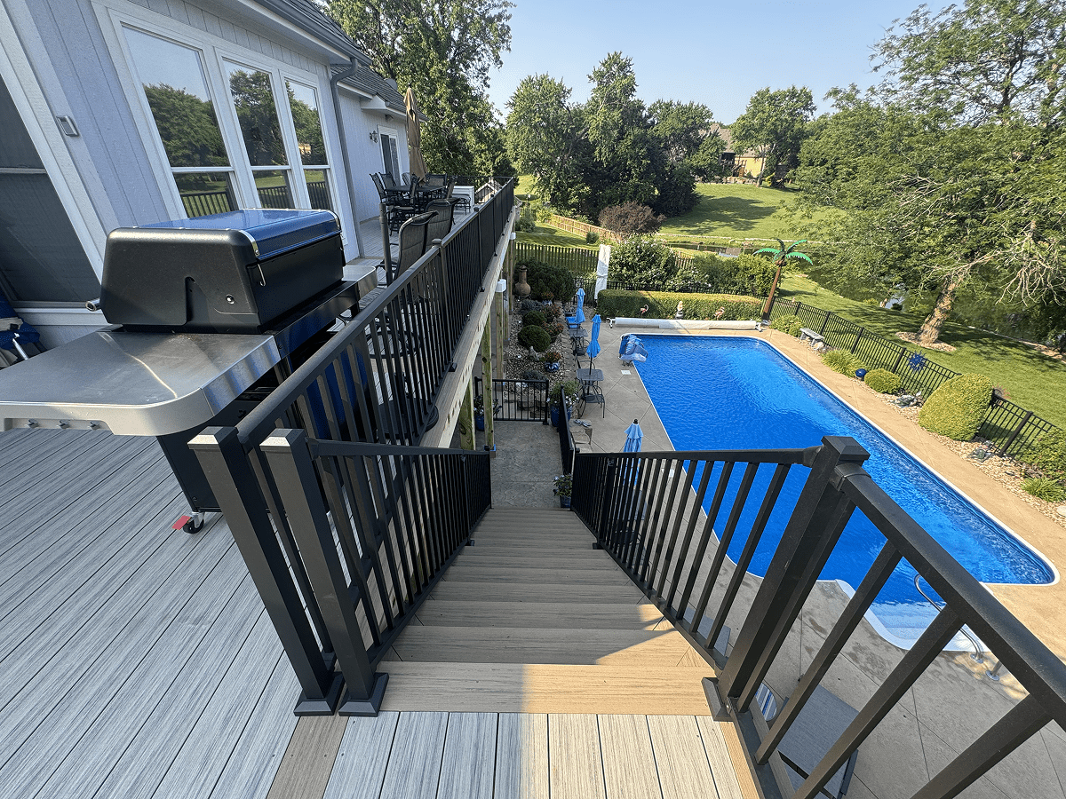 View down a staircase to a pool and garden area on a sunny day.