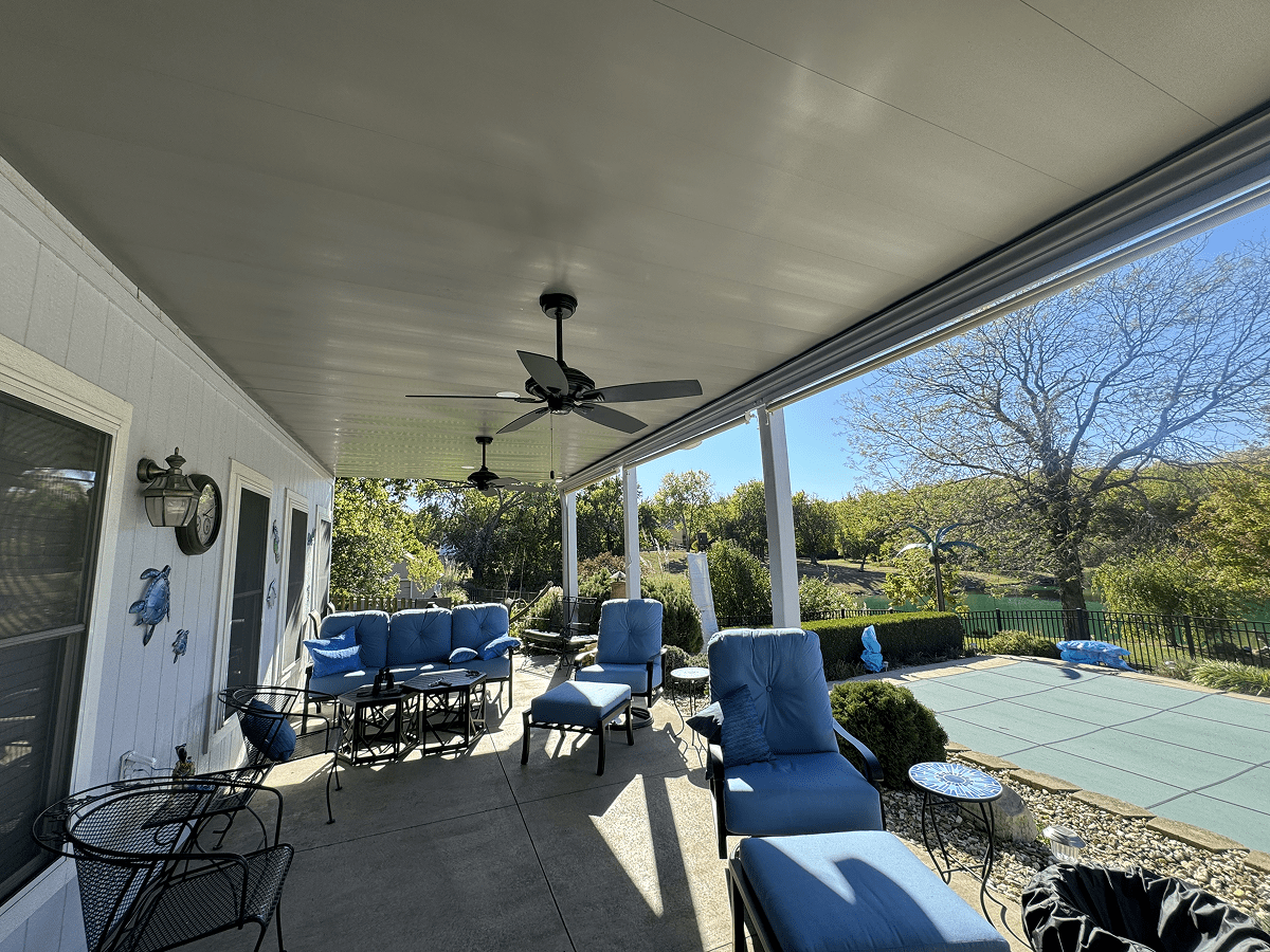 Cozy outdoor patio with blue cushioned chairs and ceiling fans overlooking a green yard.