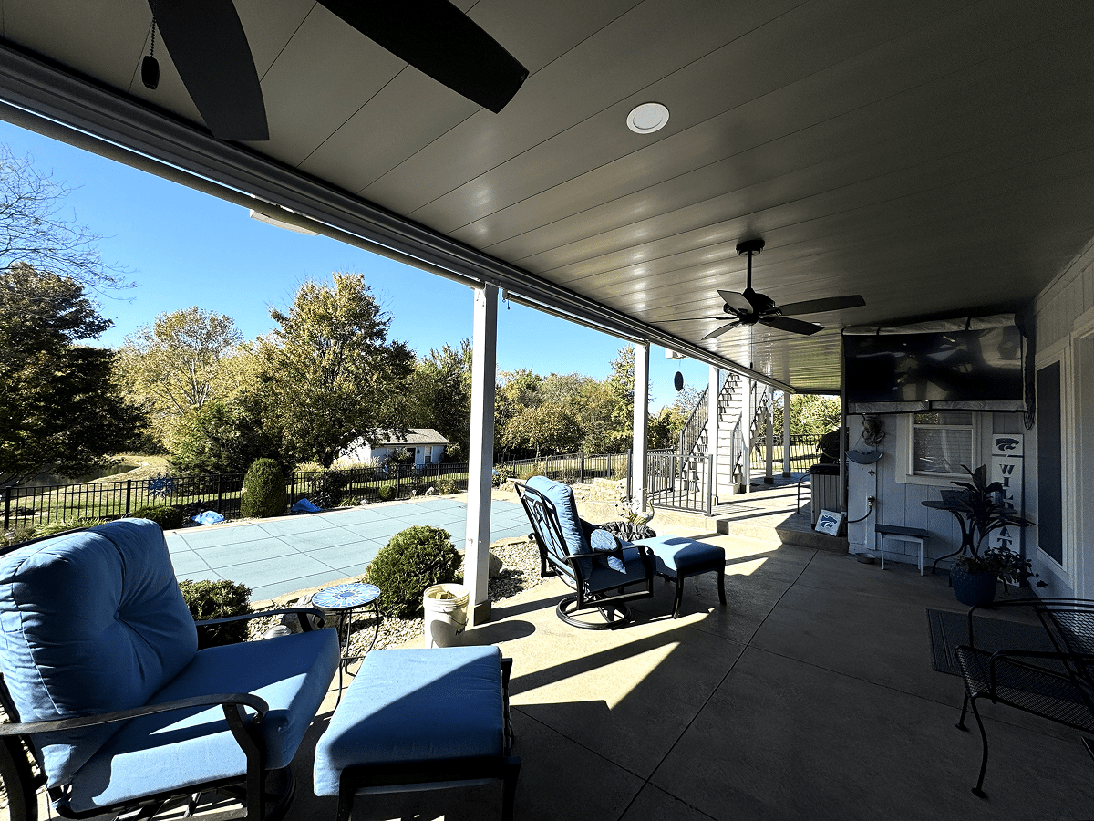 Spacious covered patio with comfortable seating and ceiling fans overlooking a green backyard.