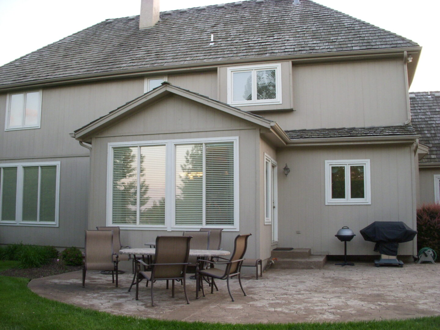 Backyard patio with outdoor dining set and barbecue grill beside a two-story house.