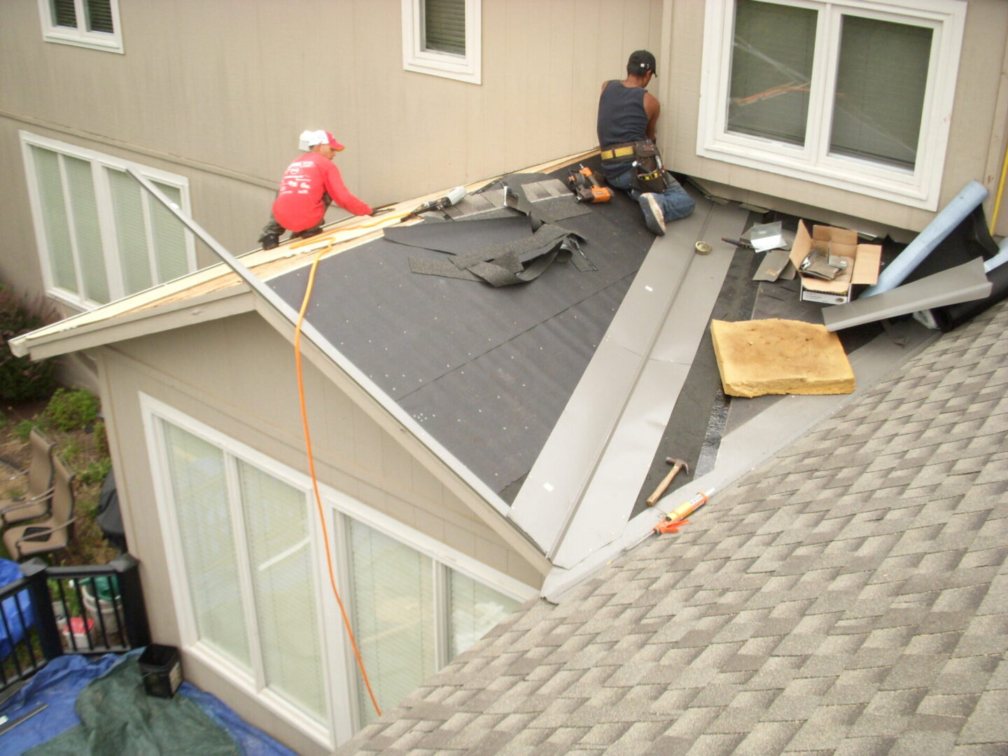 Two workers installing roofing shingles on a house roof.
