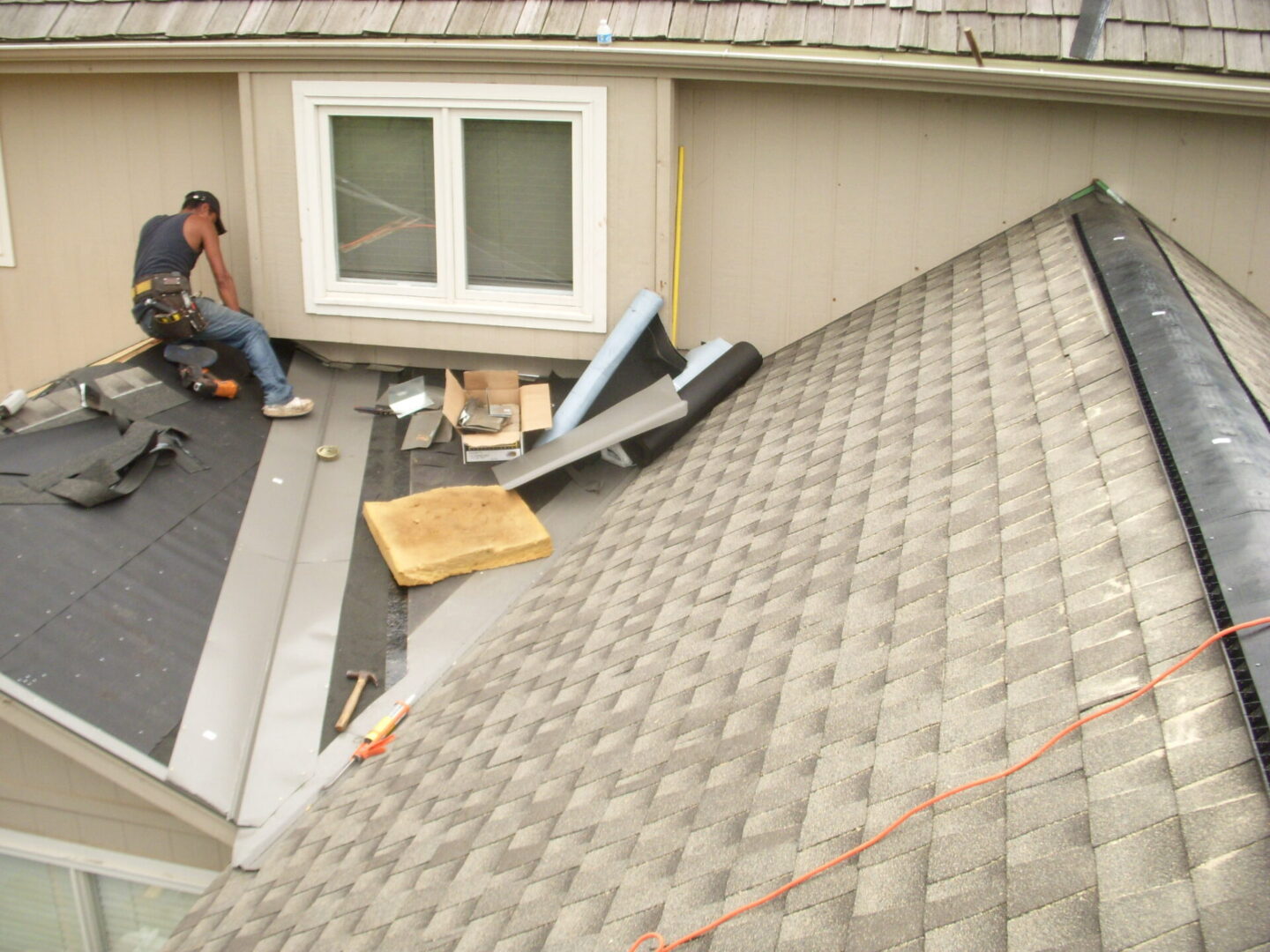 Worker repairing a residential roof with new shingles and flashing.