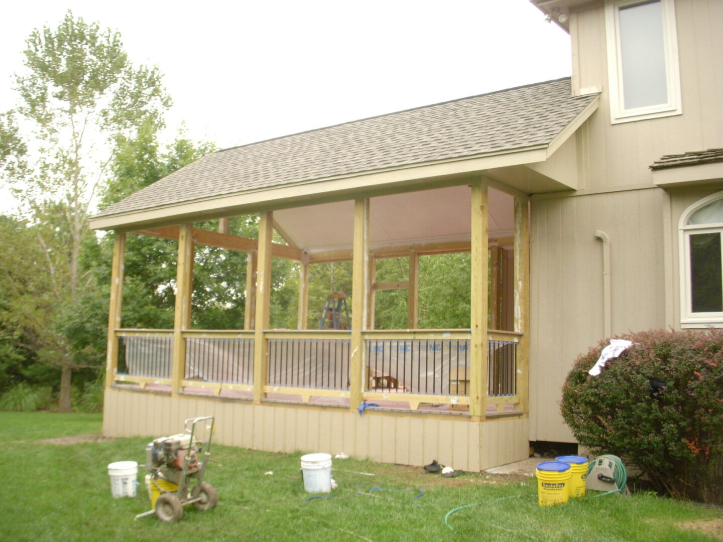 A screened-in porch attached to a house with gardening tools nearby.