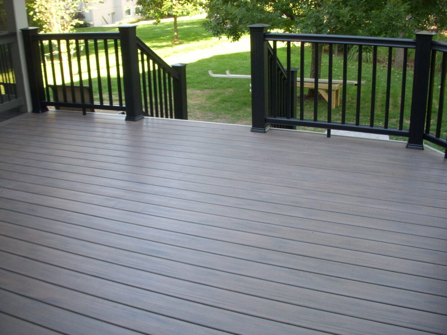 Spacious gray outdoor deck with black railings overlooking green lawn.