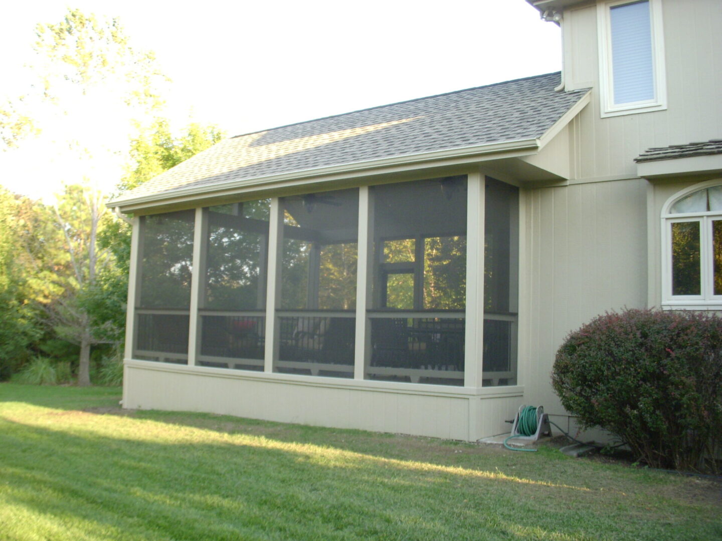 Screened porch attached to a house with a grassy lawn.