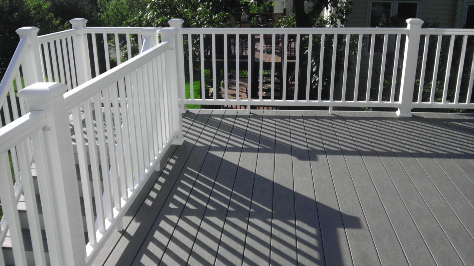 White railing casting shadows on a gray deck under sunlight.