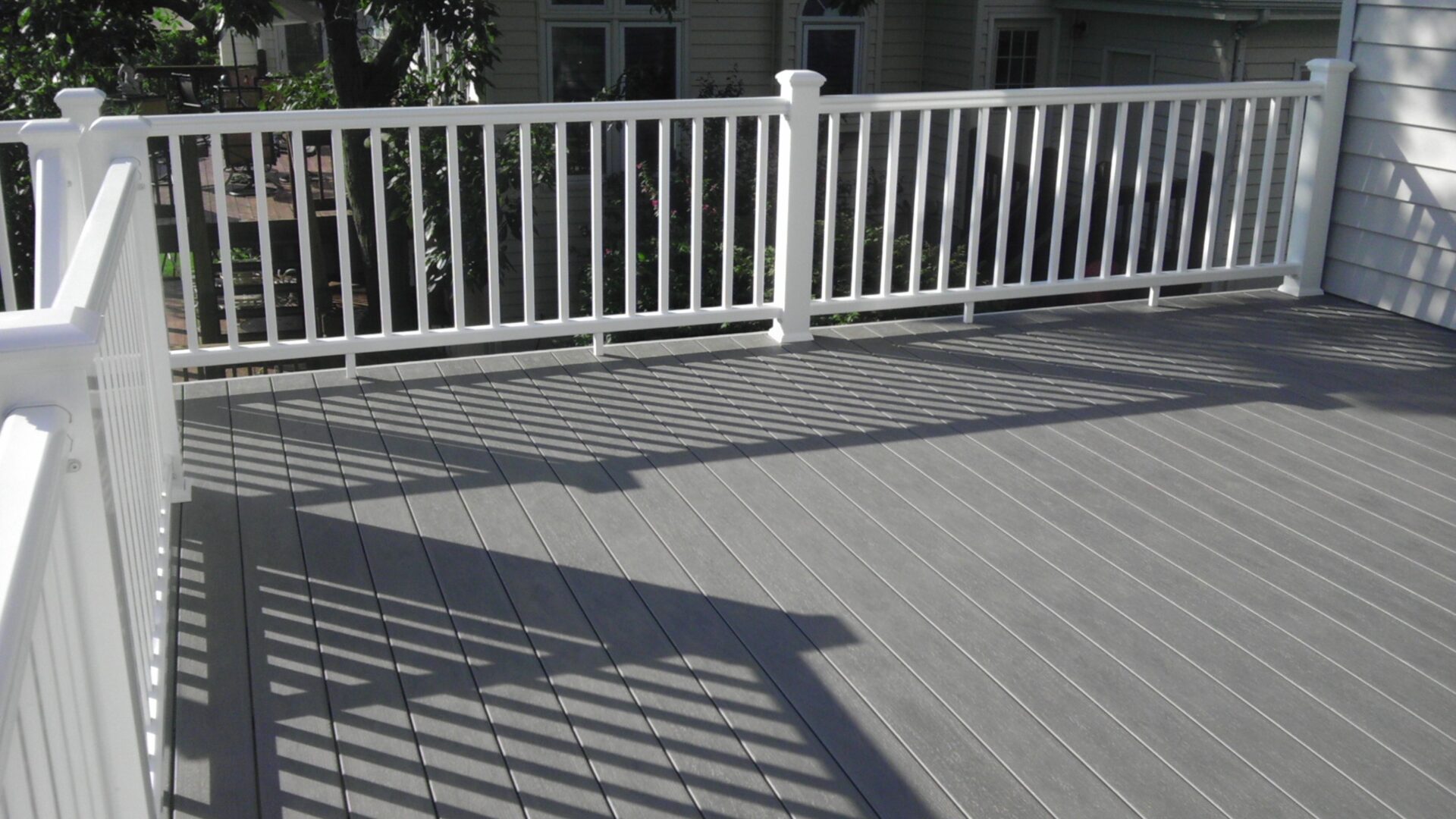 White railing casting shadows on a gray wooden deck.