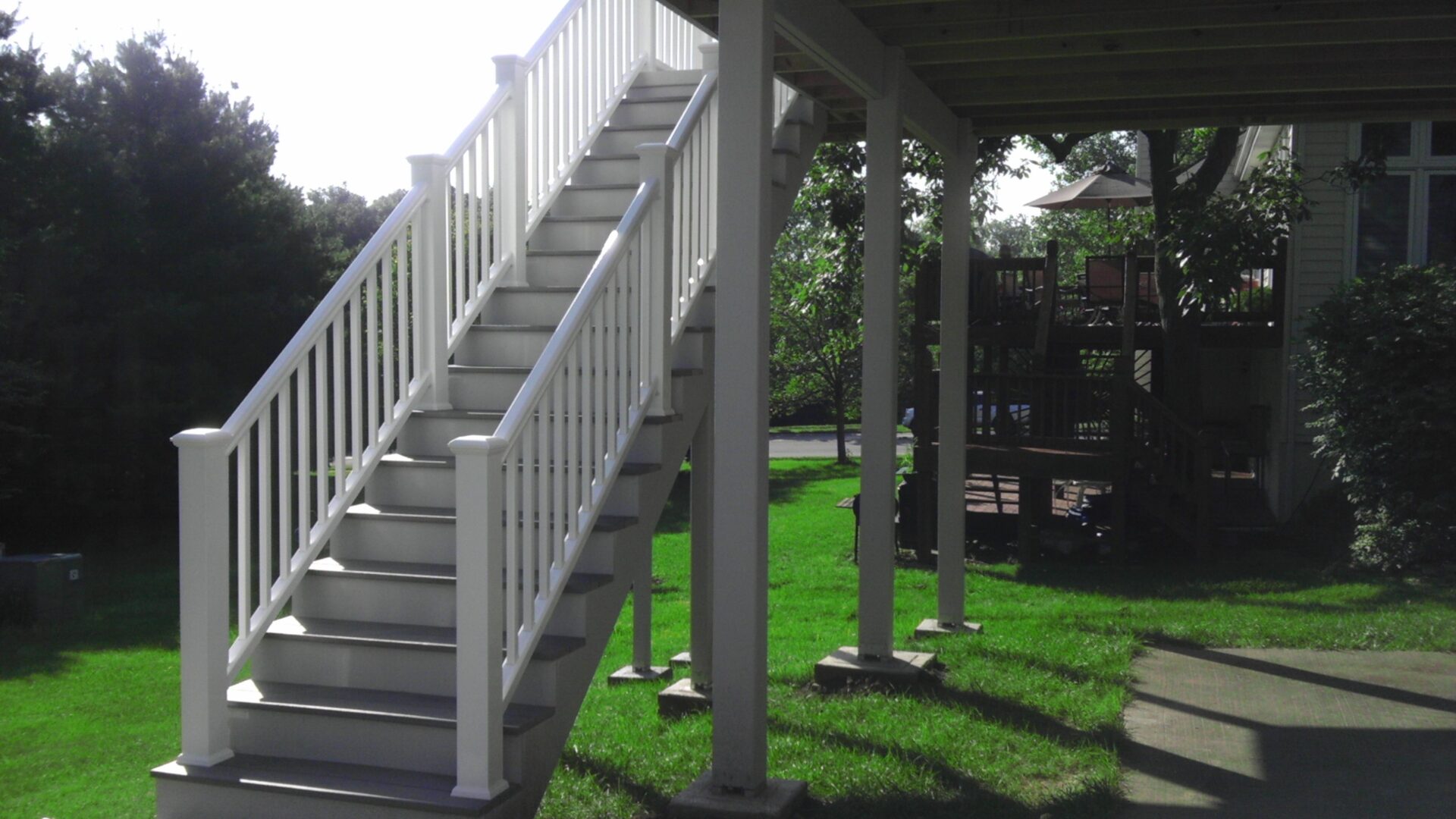 Outdoor wooden staircase leading to a raised deck in a sunny backyard.