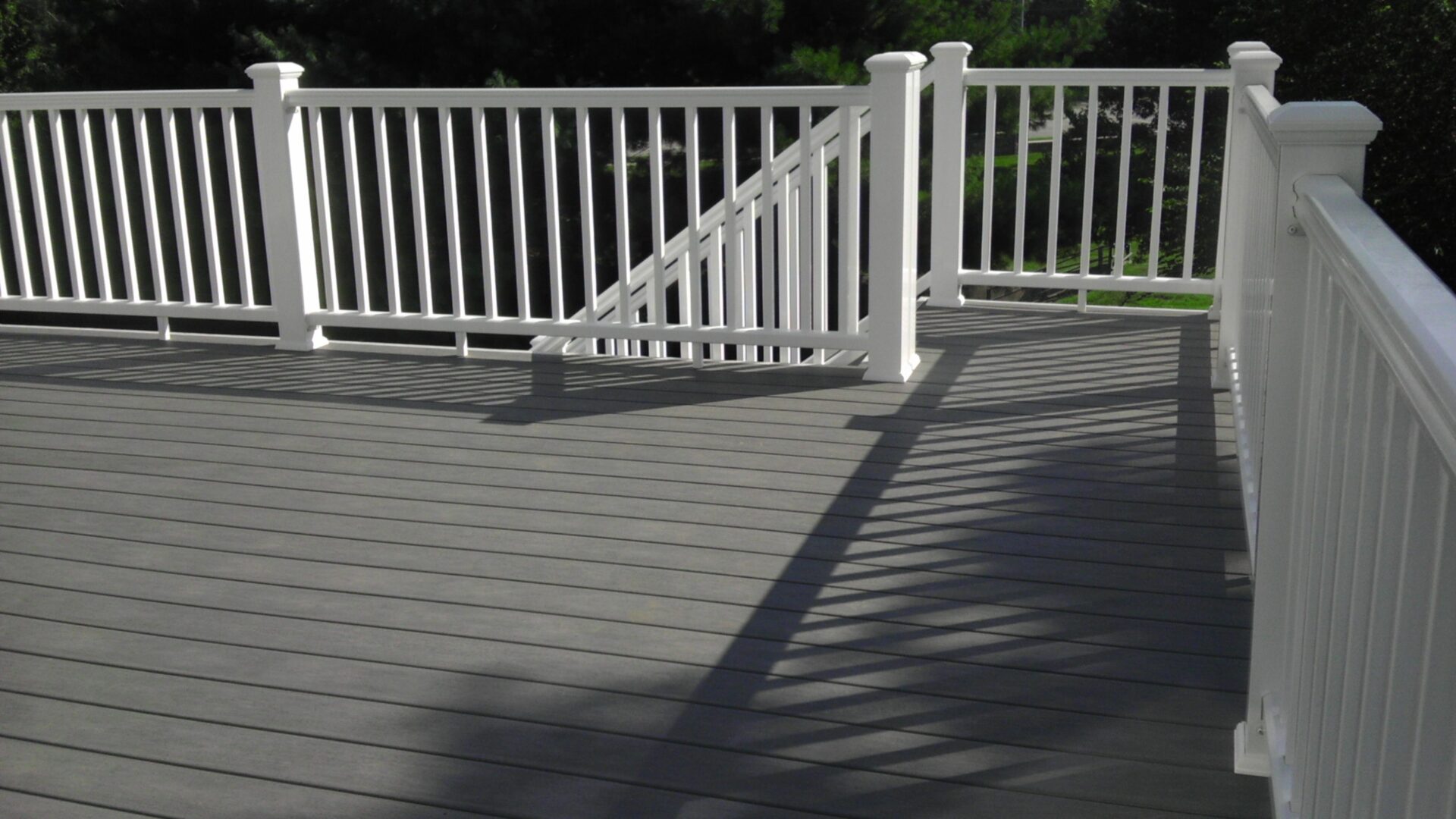 Gray composite deck with white railing and shadows in the sunlight.