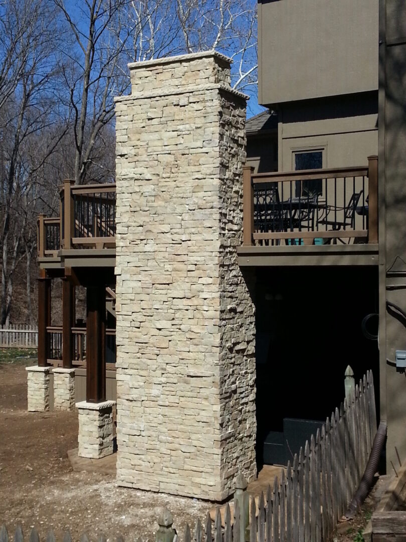 Stone chimney attached to a house with a wooden deck.
