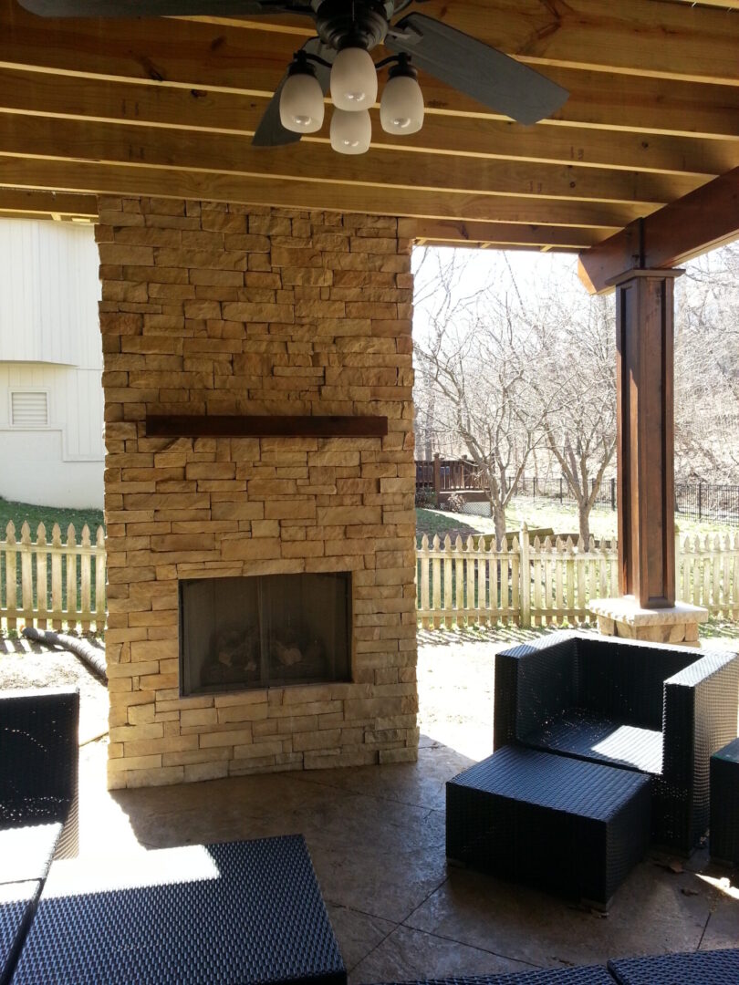 Cozy outdoor patio with stone fireplace and seating under wooden pergola.