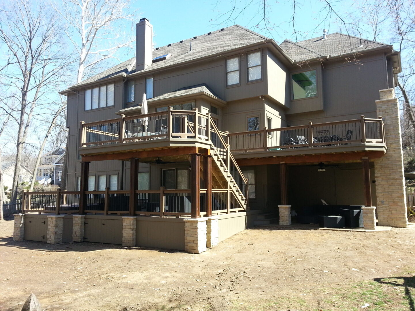 Large multi-story house with wooden deck and stairs in a backyard.